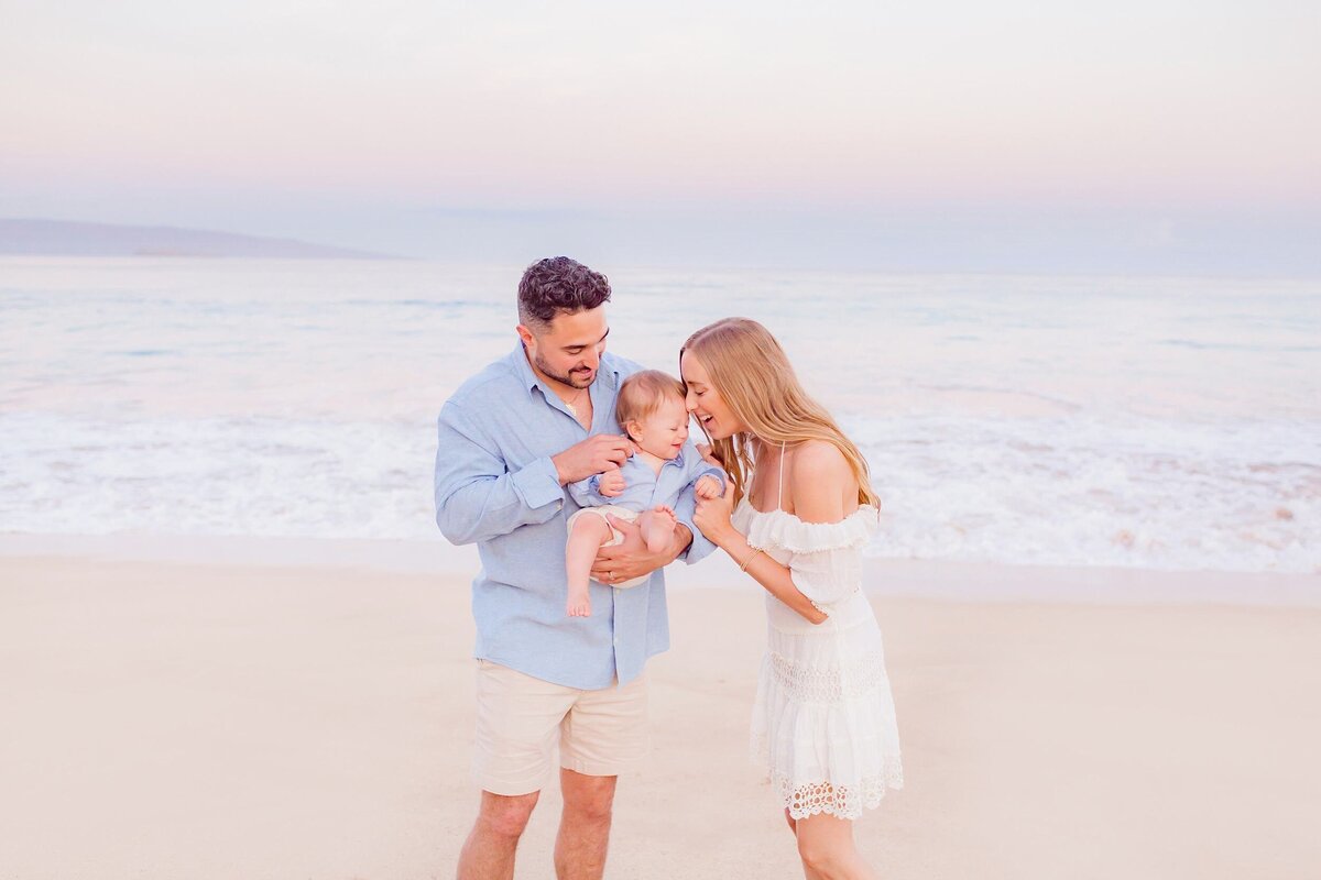 Maui family photography with young couple kissing and admiring their son next to the ocean