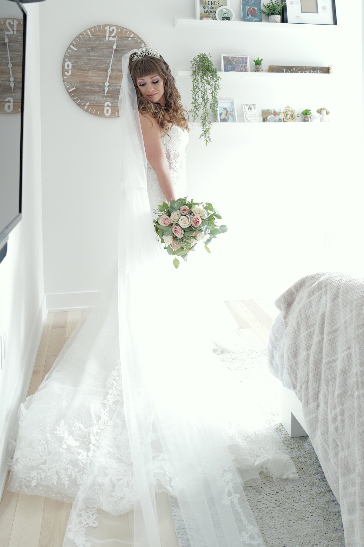 A bride stands gracefully in her wedding dress within a beautifully decorated bedroom. This image captures the elegance and intimacy of the moment, showcasing the bride's stunning gown and the serene atmosphere of her preparation space.