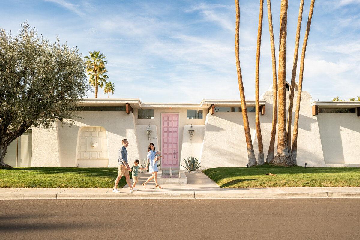 A family of four walking in front of the "pink door" house in palm springs. 
