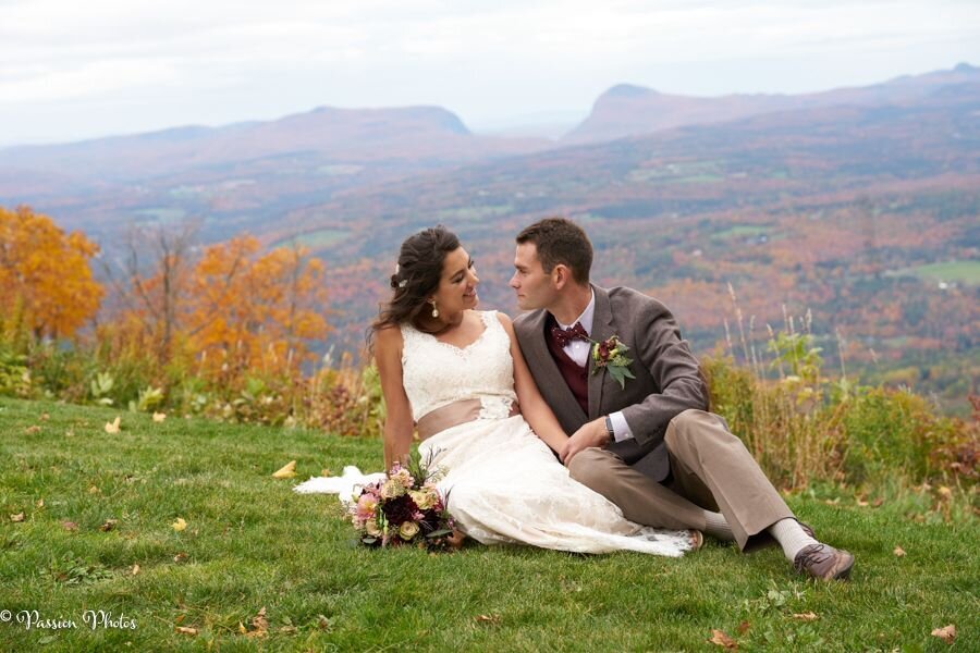 A couple sits together in a serene field, surrounded by tall grass. They appear relaxed and happy, enjoying a peaceful moment in nature. The setting emphasizes their connection and the tranquility of their surroundings.