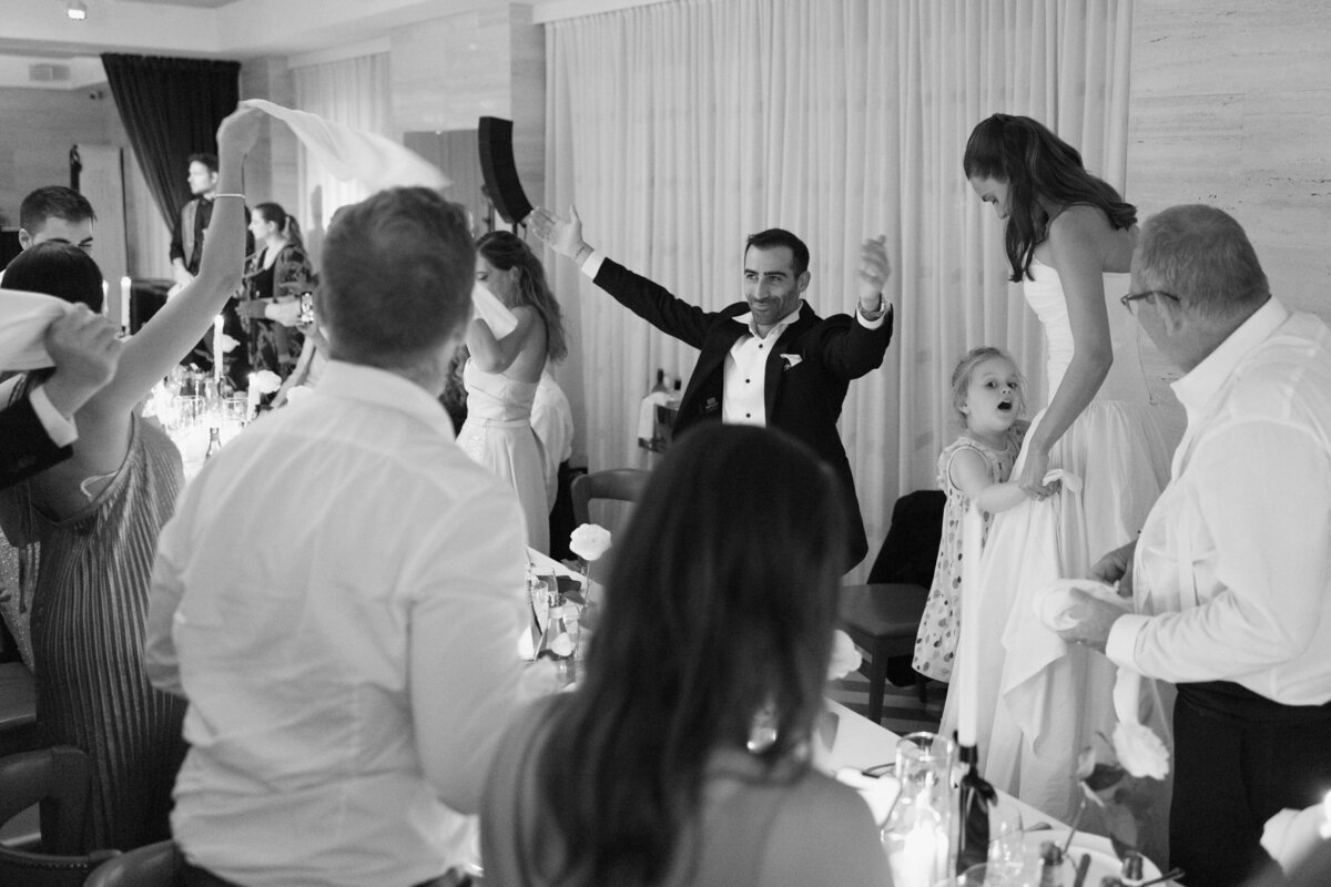 Groom and guests waving napkins during joyful dinner celebration


