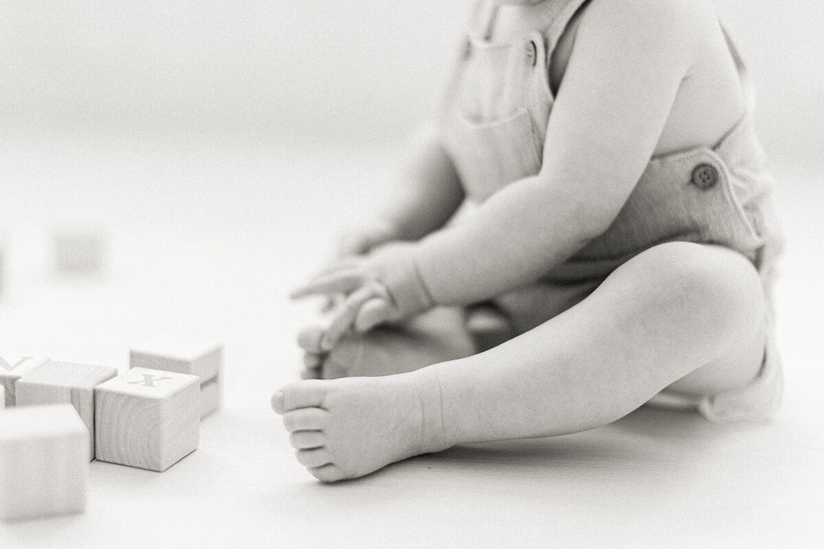 A close up black and white photo of a little baby boy playing on a DFW photography studio floor with wooden blocks.