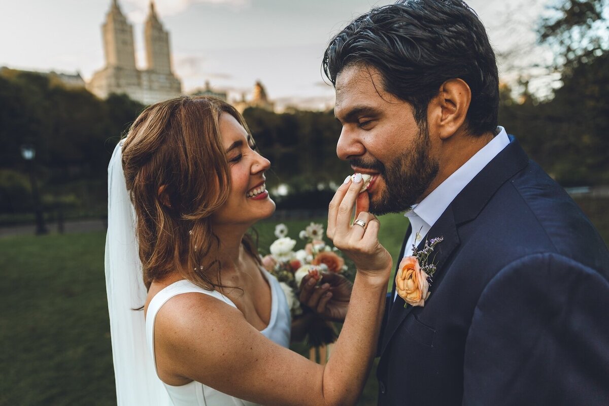 Bride laughing and feeding groom a macaron during picnic