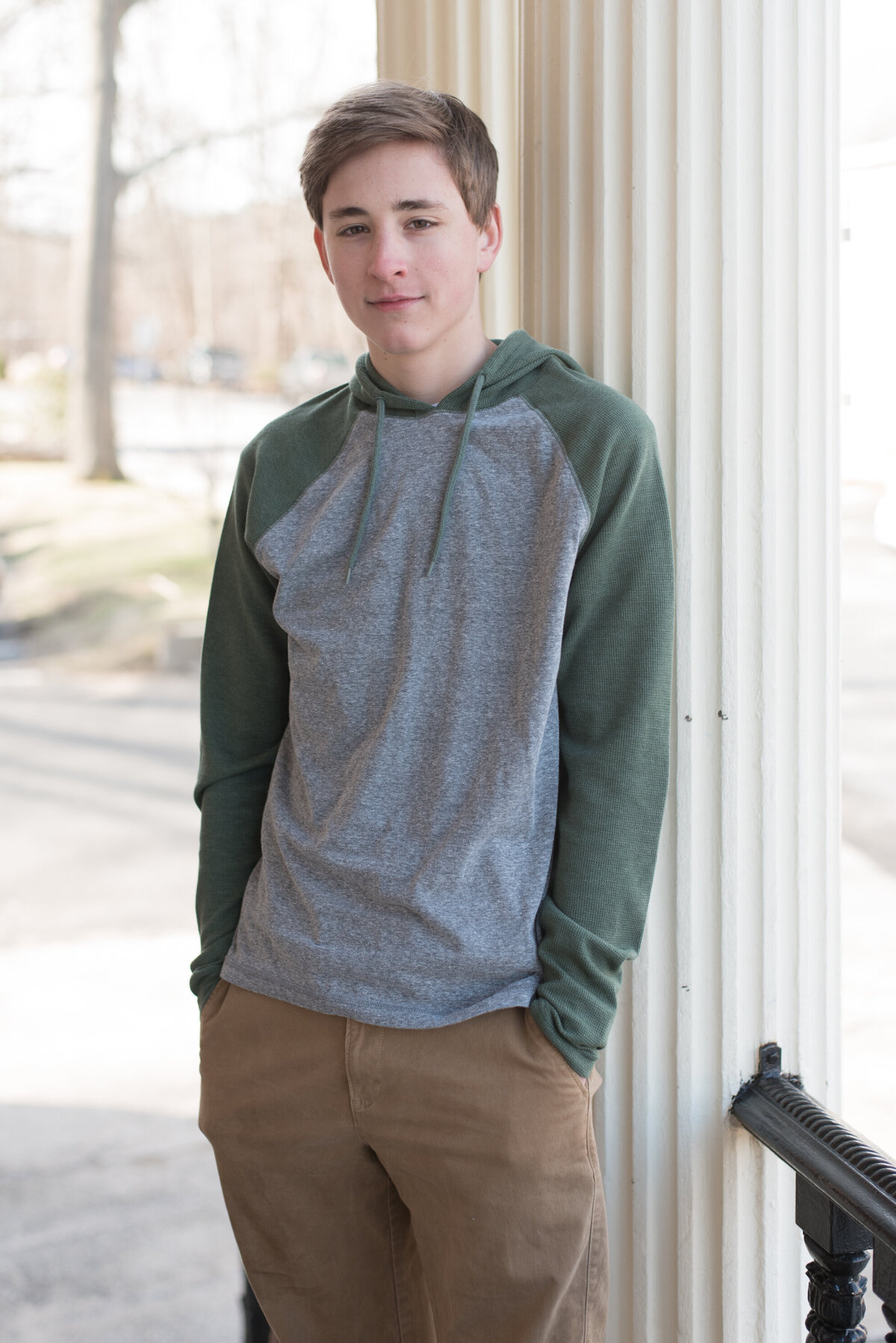 Teen boy with hands in pockets in front of white column