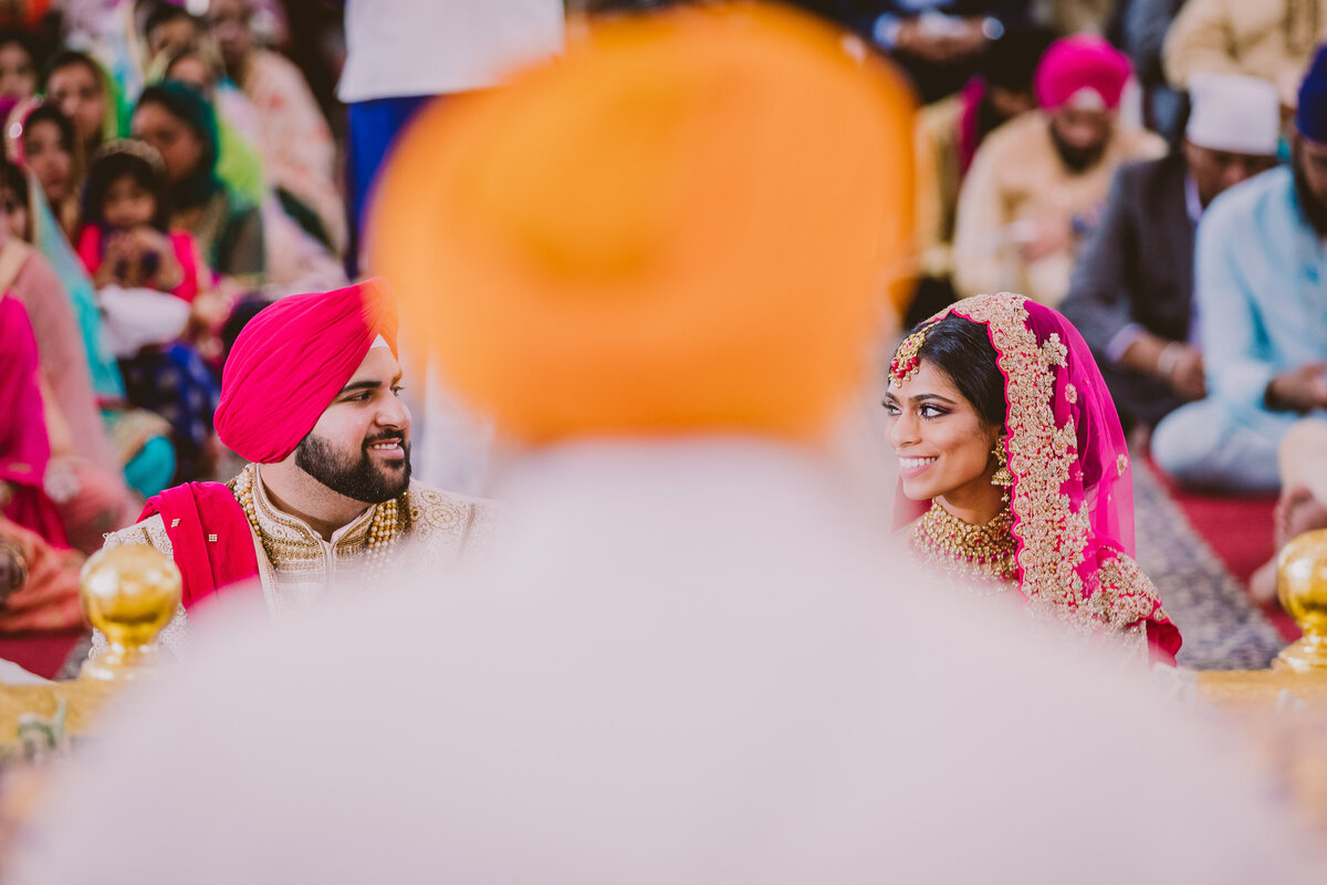 A sikh couple smiling at each other during their anand karaj wedding ceremony