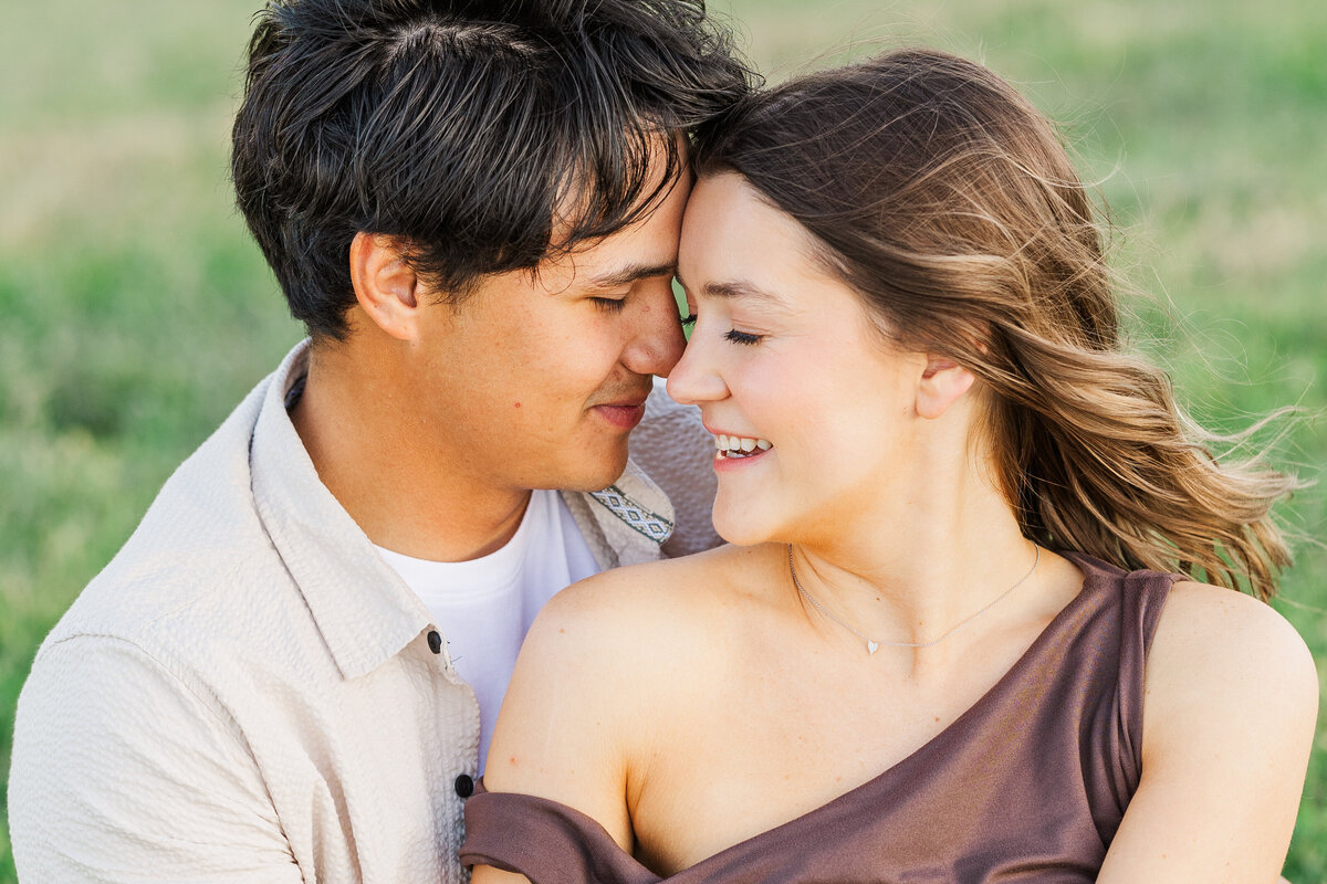 Authentic and joyful engagement photo of a couple in downtown Fort Worth. Captured in a close embrace with eyes closed and noses touching, their laughter and connection radiate love and warmth on a breezy Texas afternoon.