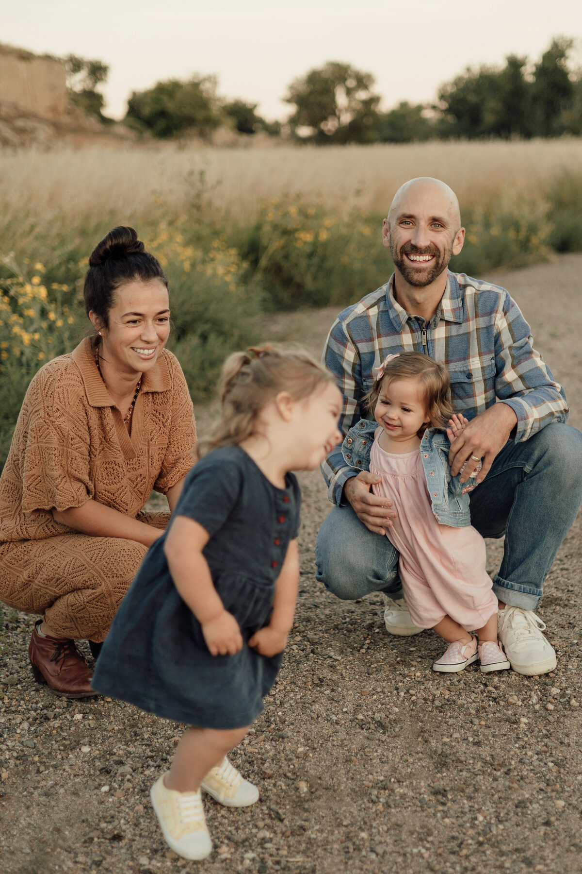 family of four looking at older daughter running around laughing during lifestyle family session at sandstone ranch in longmont colorado with alexis adkins photography