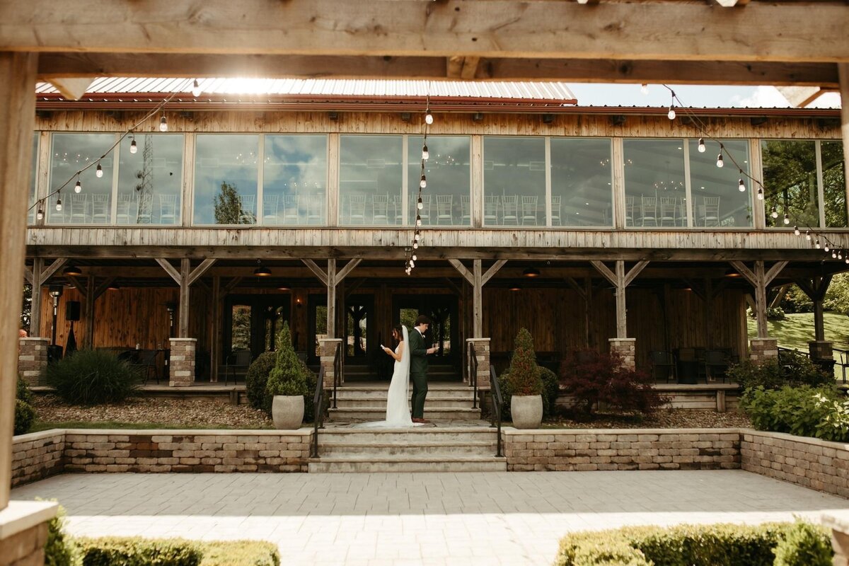 a bride in a long white gown and a groom in a blue suit have a first look moment on the stone courtyard patio at Willowbrook wedding venue