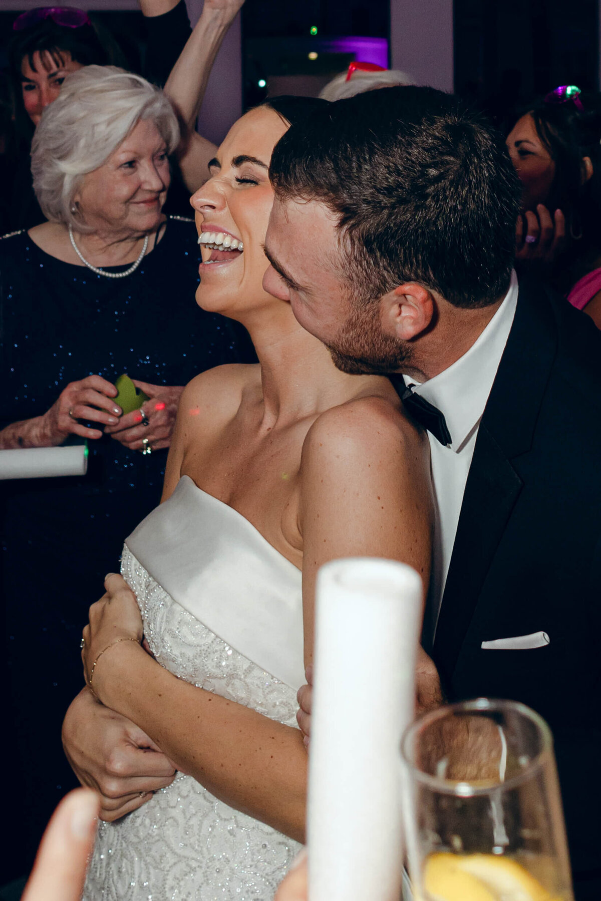 A candid wedding photo of the groom kissing the bride while she smiles and laughs