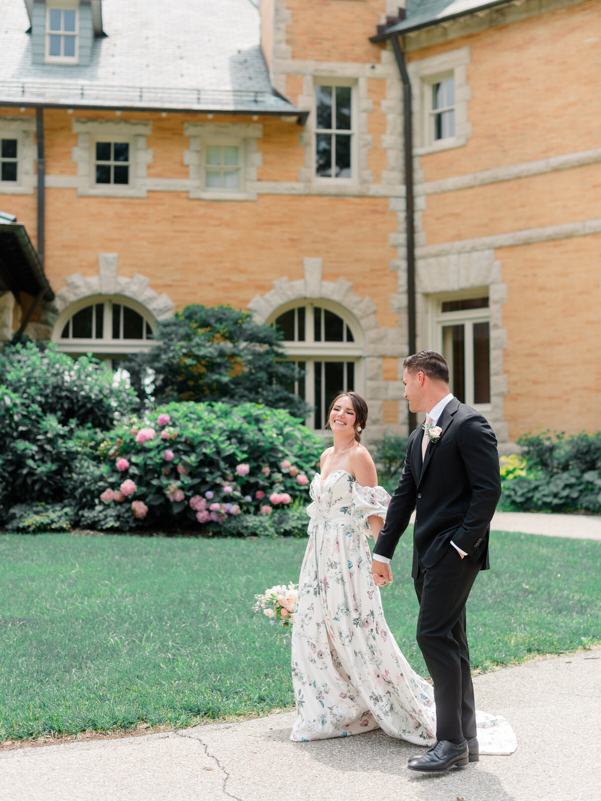 Joyful bride and groom walk hand-in-hand through the lush grounds of Cairnwood Estate, captured by Elizabeth Kane Photography, a leading Philadelphia Fine Art Wedding Photographer. This editorial moment highlights refined romance, timeless bridal fashion, and the elegant architecture of one of Pennsylvania’s most iconic luxury wedding venues.