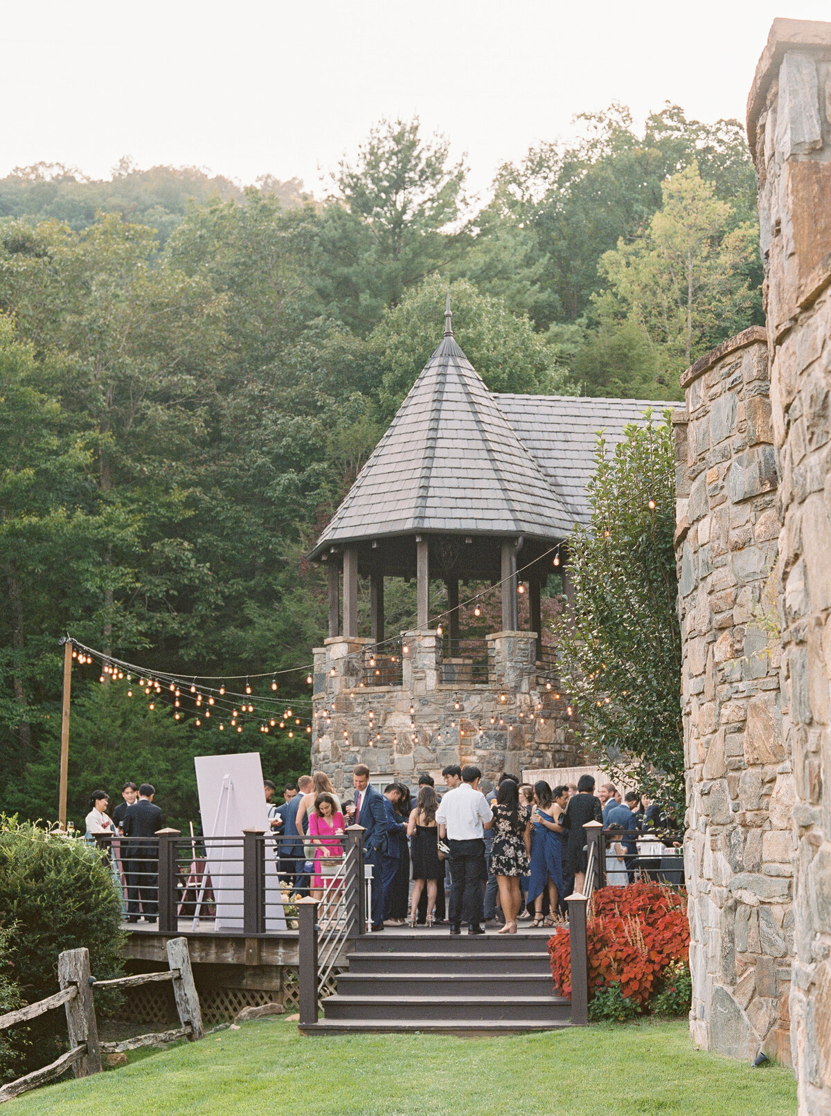 Guests mingling during cocktail hour on wooden deck surrounded by forest at Castle Ladyhawke in North Carolina.