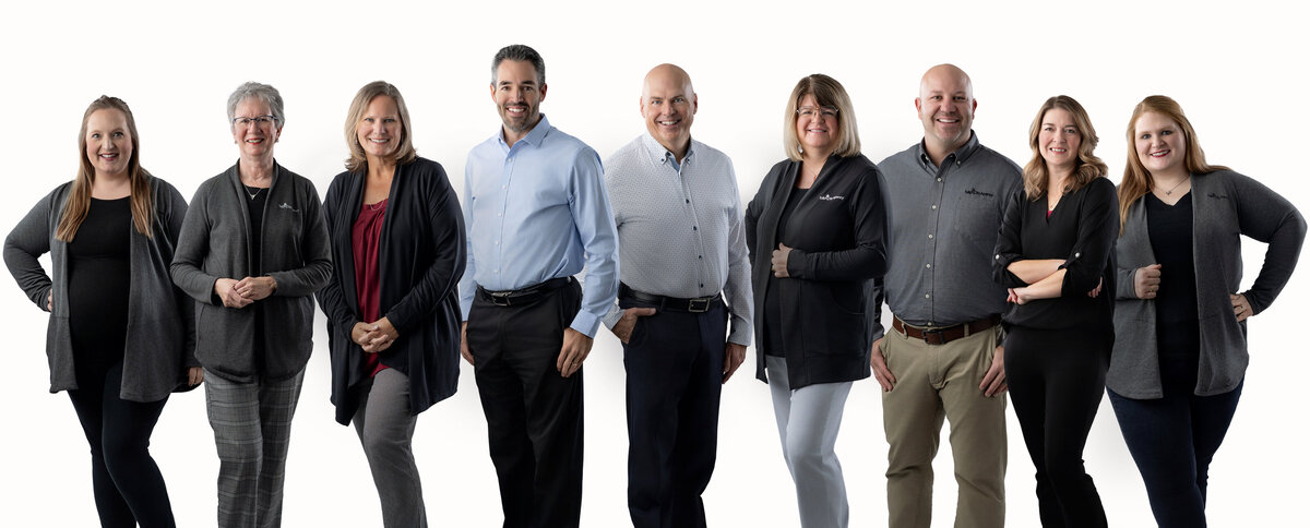 A group of 9 people stand side by side on a white background in their full business headshot composite. 