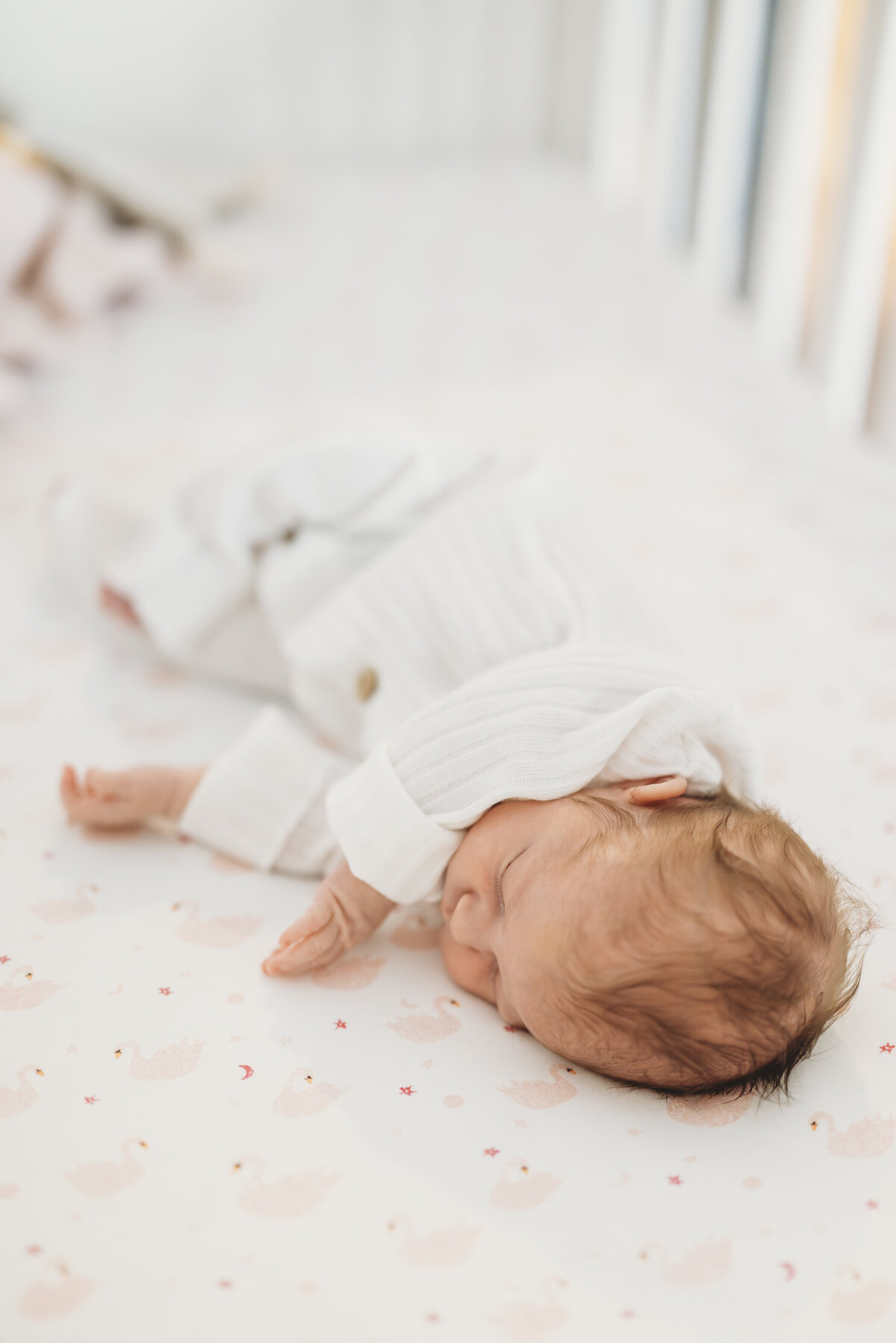 Newborn baby sleeping on their back in a white onesie, photographed in a softly lit nursery by a Kansas City newborn photographer.