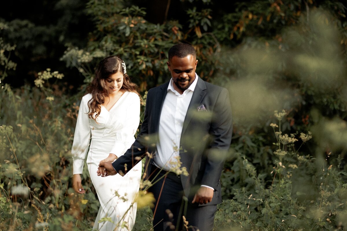 Happy couple wearing wedding attire walking in grass at Pergola and hill garden-1635
