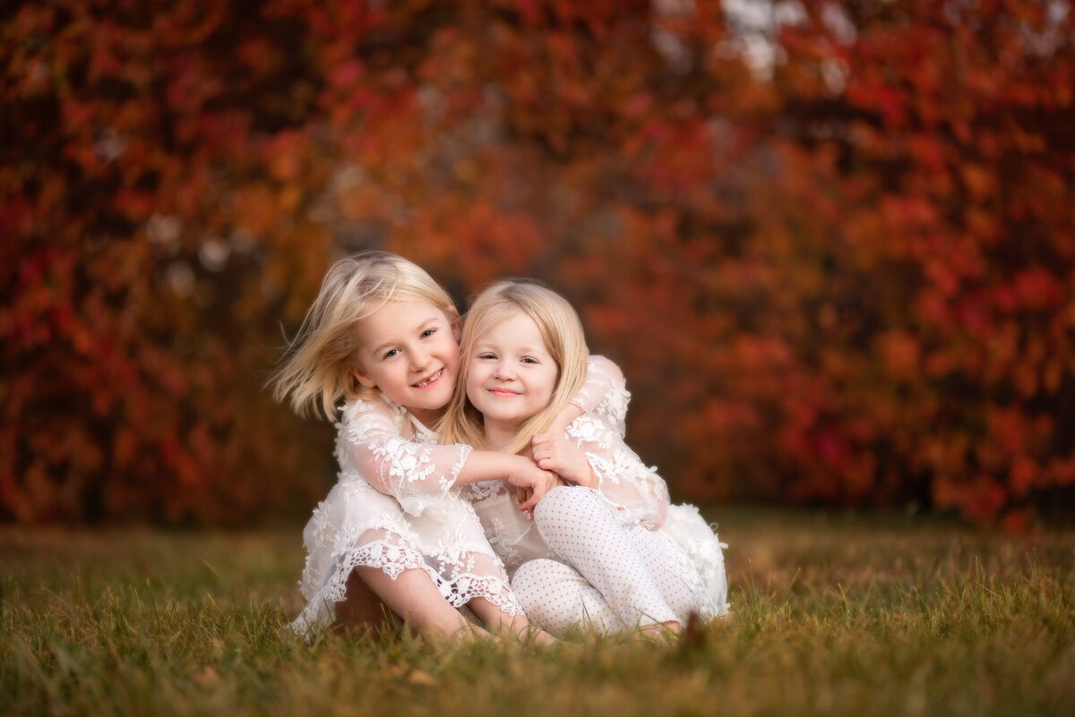 Heartwarming outdoor portrait of two siblings hugging in a field surrounded by vibrant autumn colors. Captured in Lenexa, Kansas, this candid setup is ideal for families seeking seasonal sibling photography