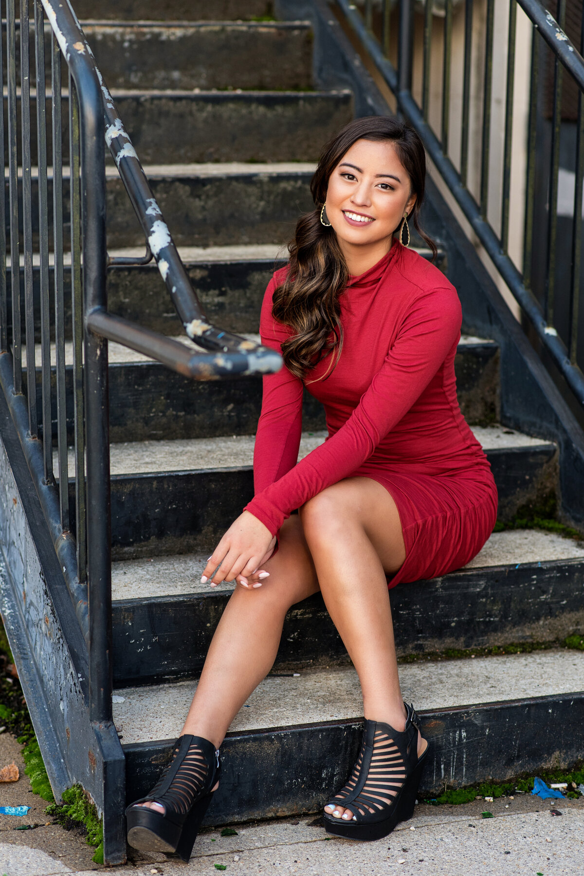 High school senior girl wearing red dress poses on staircase downtown Richmond, VA.