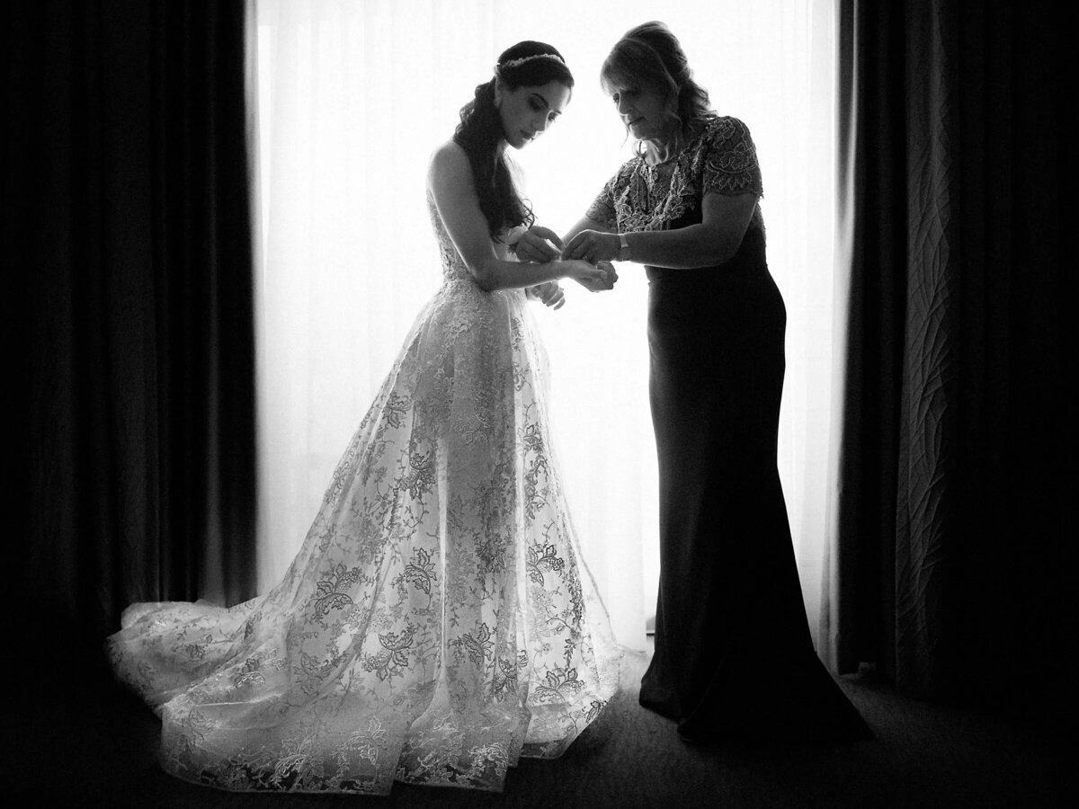 A black and white photo of a bride receiving assistance with her dress