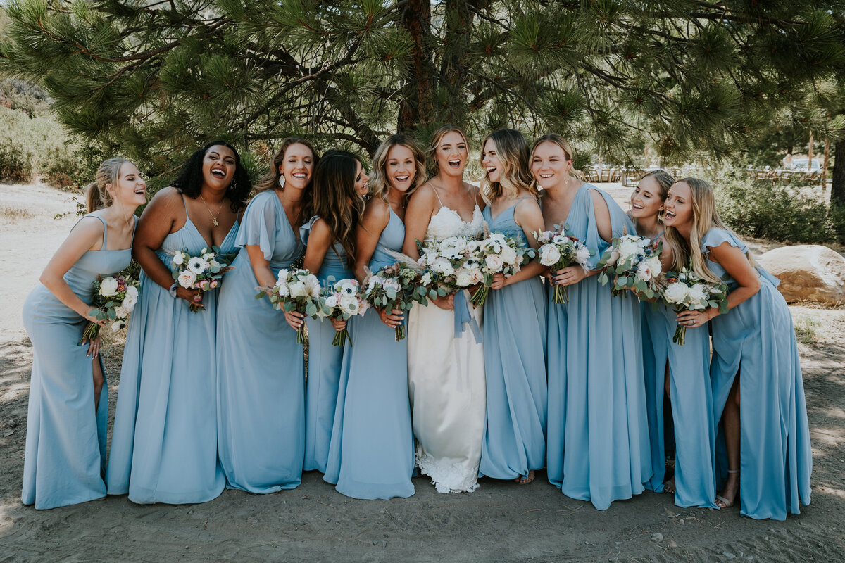 Bride and bridesmaids laugh together while holding bouquets.