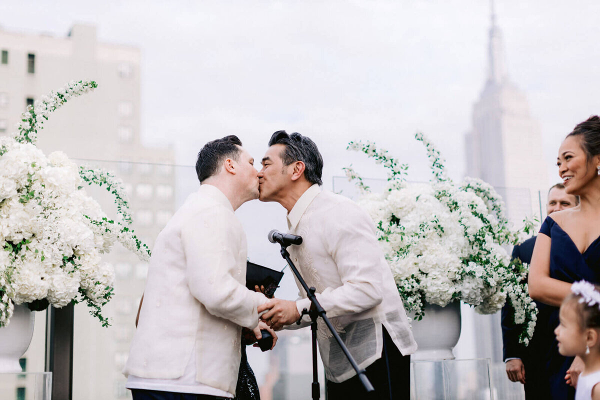 Two grooms kiss in the wedding ceremony in The Skylark, New York. Wedding Image by Jenny Fu Studio