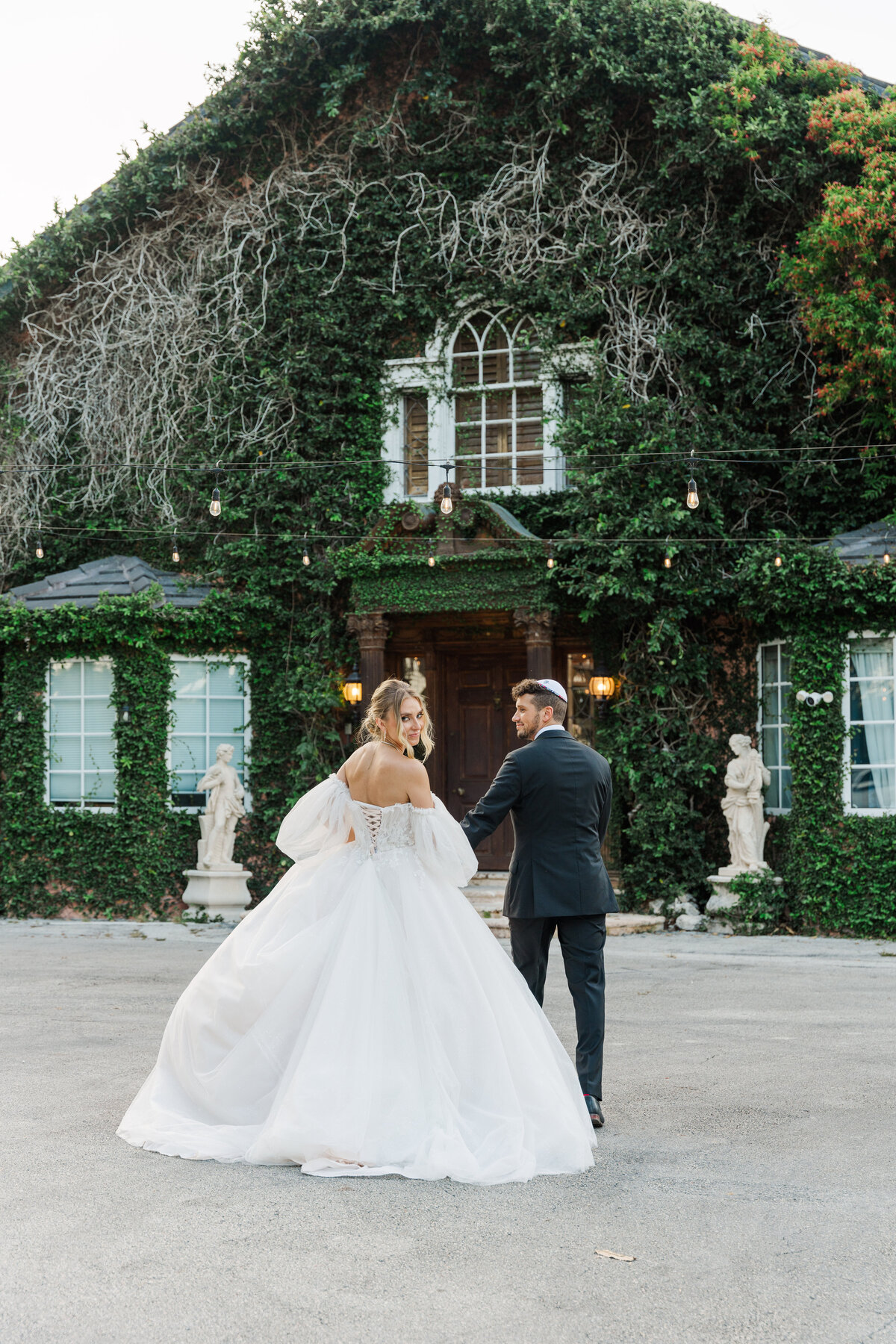 bride and groom walking away frm the camera while she looks bak at it