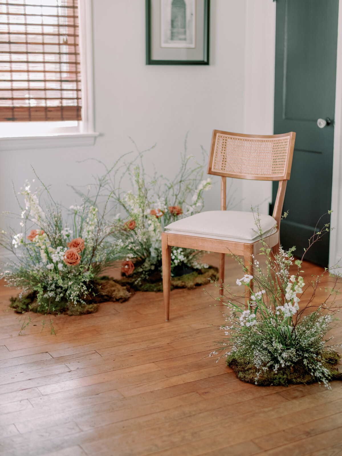 A wicker chair is surrounded by three floral arrangements indoors.