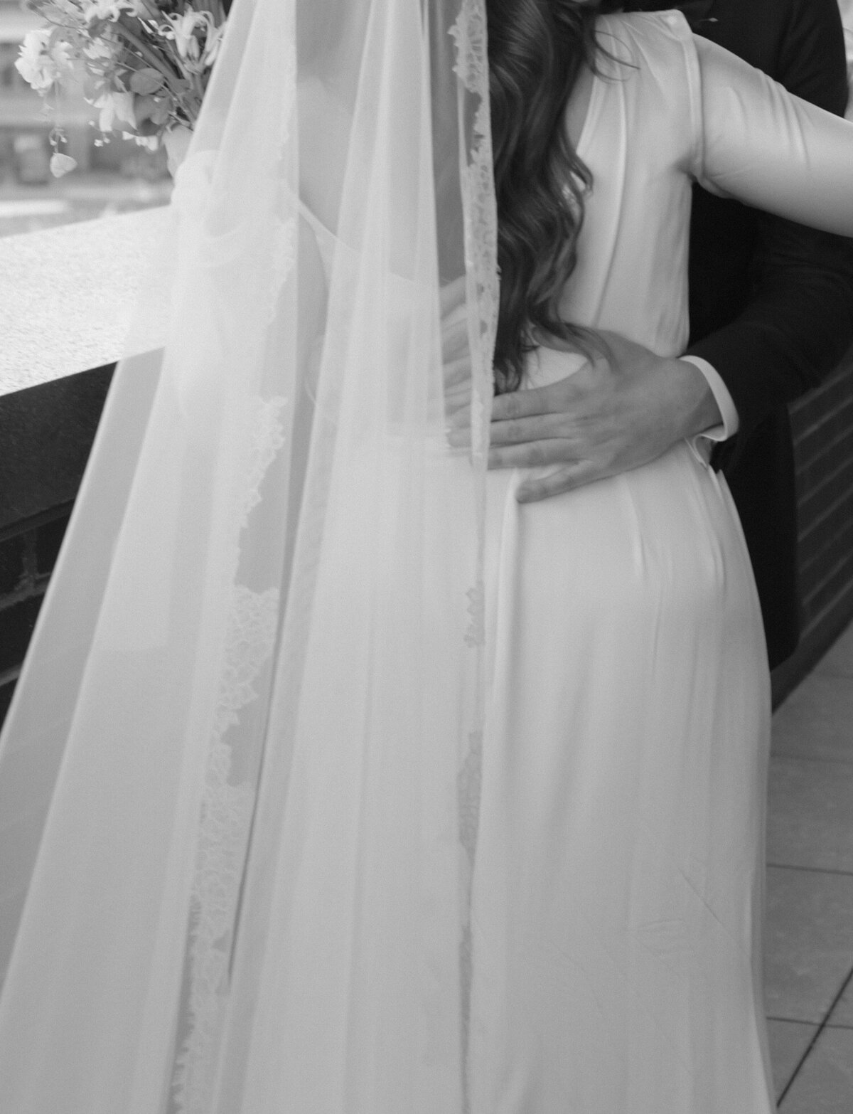 close, soft, candid black and white wedding photography of a groom's hands hugging his bride at Shinola Hotel
