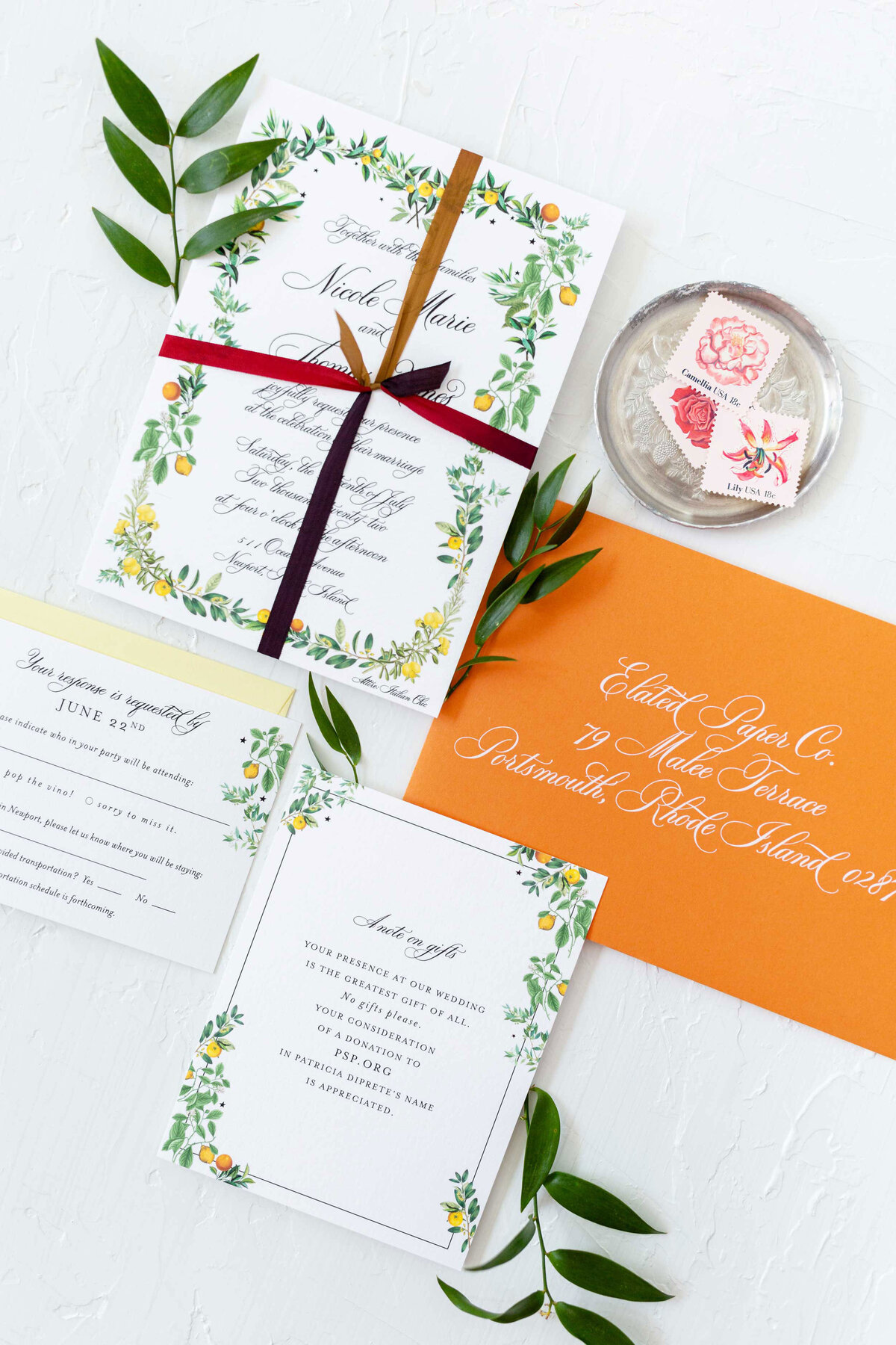 Mediterranean inspired invitation suite with lemons and oranges. Orange Envelope with white ink addressing. Favor card with touches of lemons and oranges and leaves. Flat lay composition