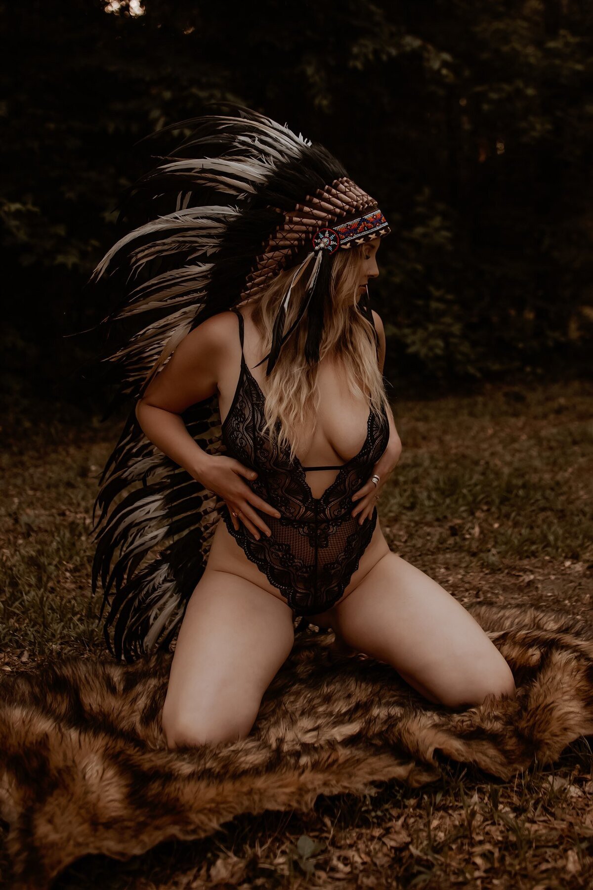 Liberty, Tx blond woman kneeling on a fur rug in the woods in black bodysuit