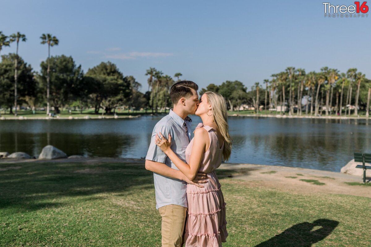Engaged couple share a sweet kiss in front of the Mile Square Park pond