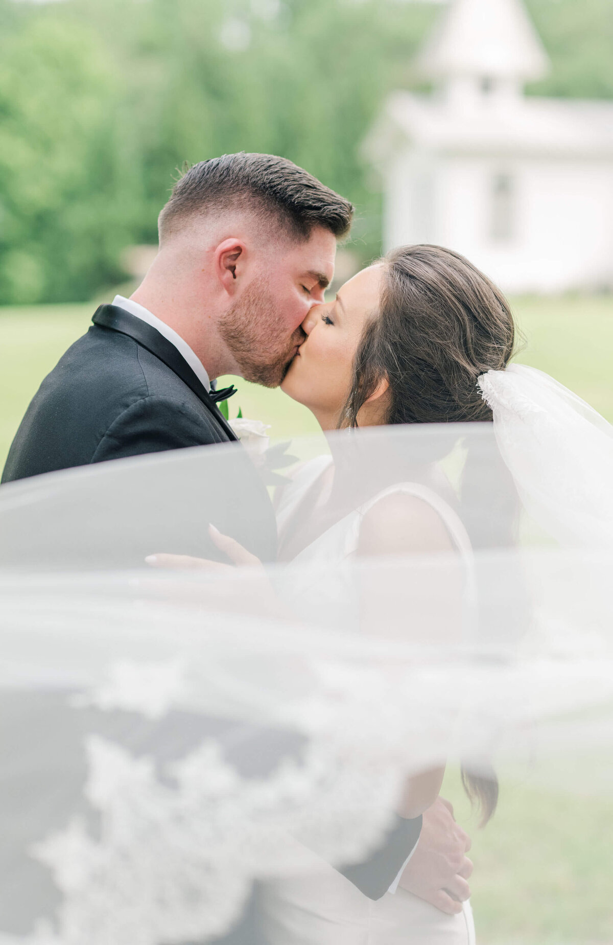 Bride and groom kissing with veil flowing in front of them