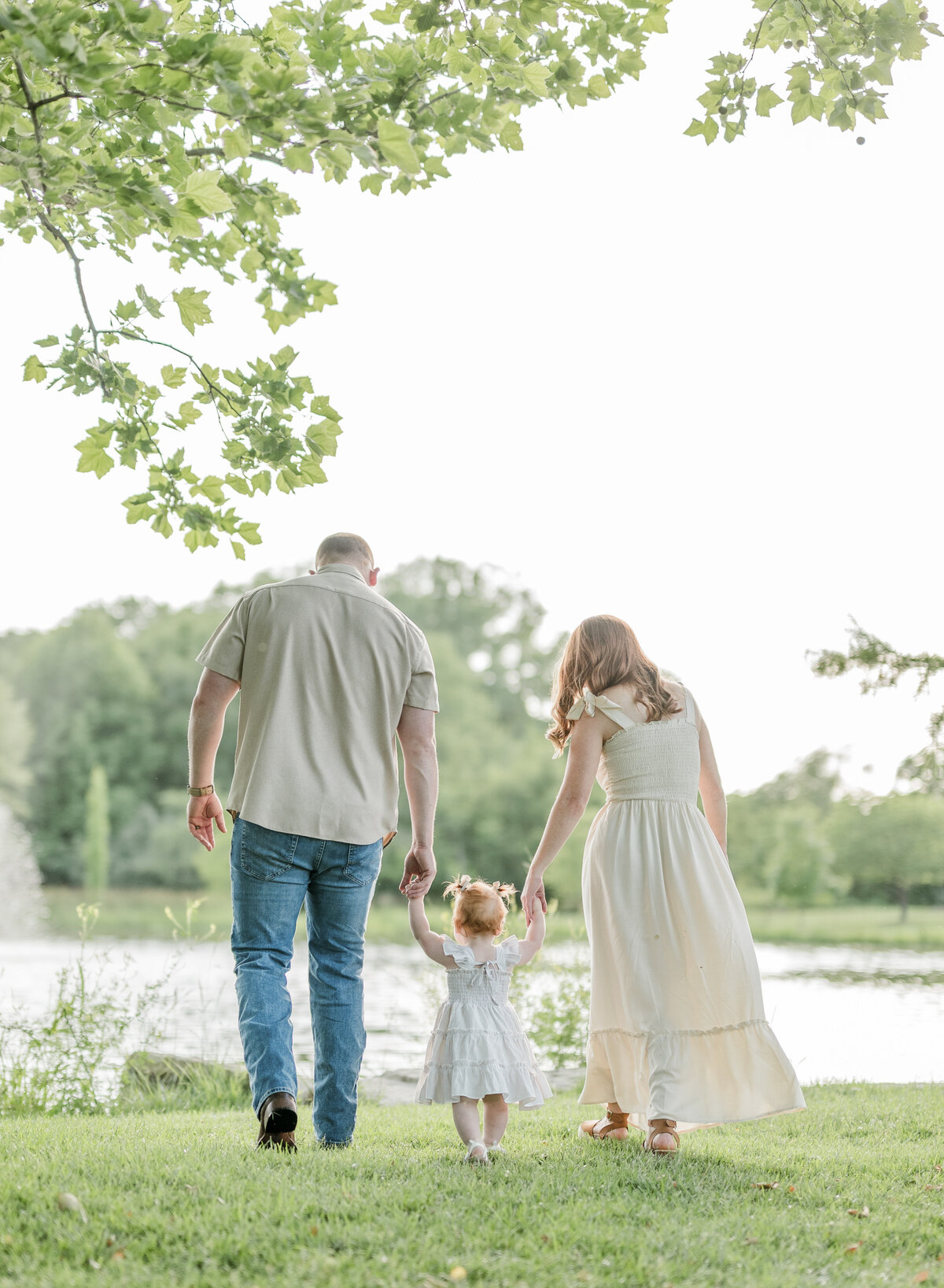 Family walking hand-in-hand in a grassy park near the lake during a lifestyle photography session in Kansas City.