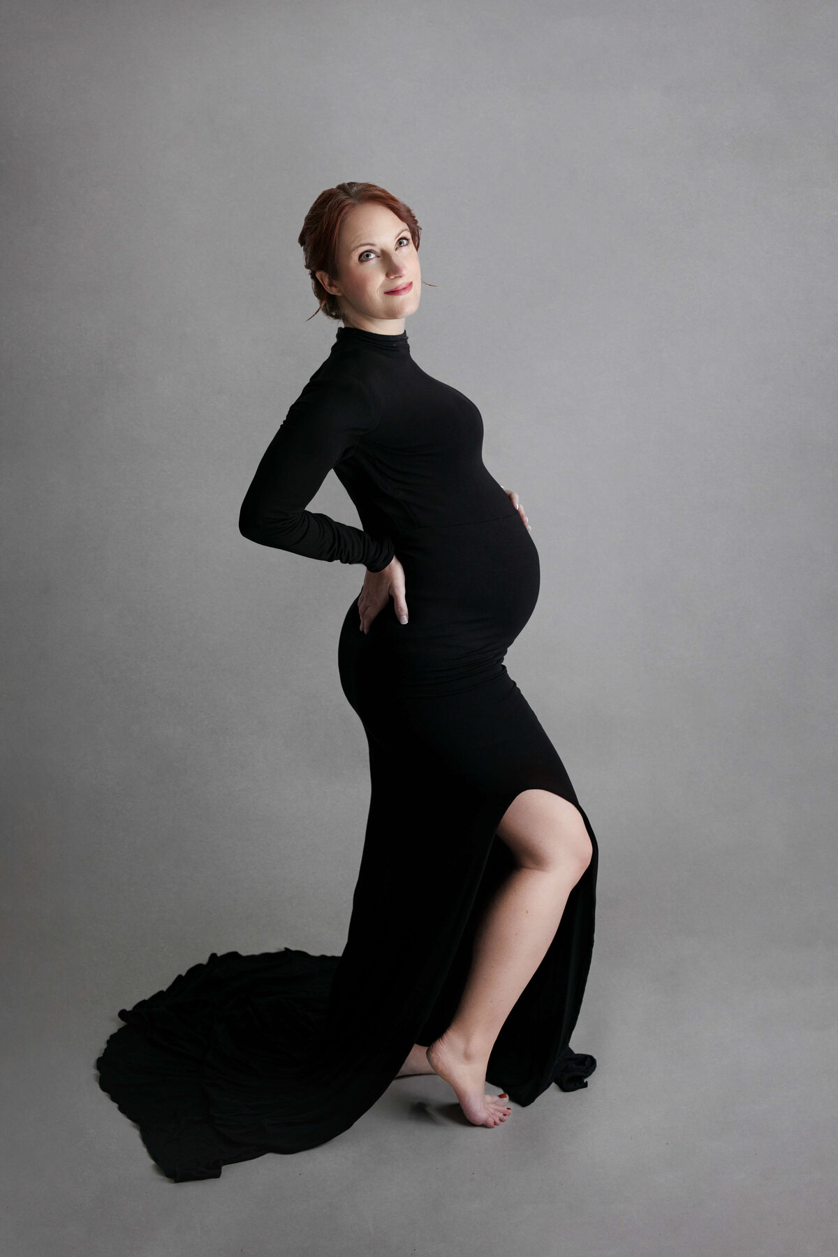 pregnant woman looking up holding her back in a black maternity gown in a photography studio