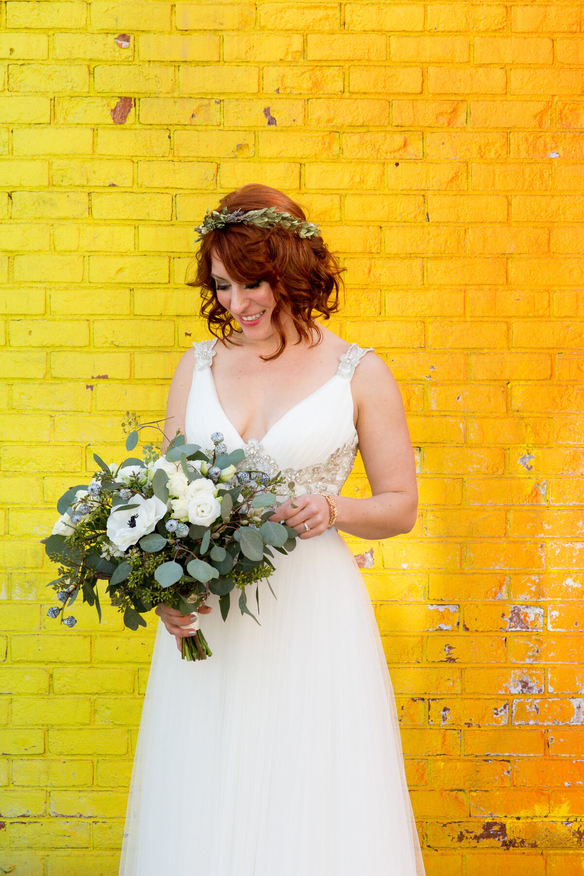 A bride holding her bouquet while standing in front of a bright wall.