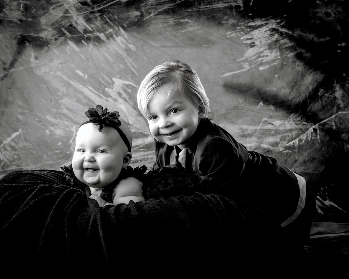 A brother and sister lay on a rug together in Black and White