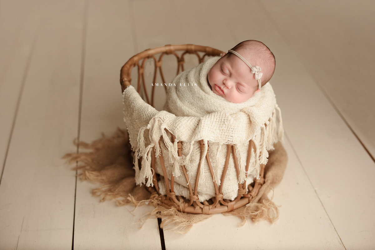 Luxurious newborn portrait of baby in beige sheets and basket