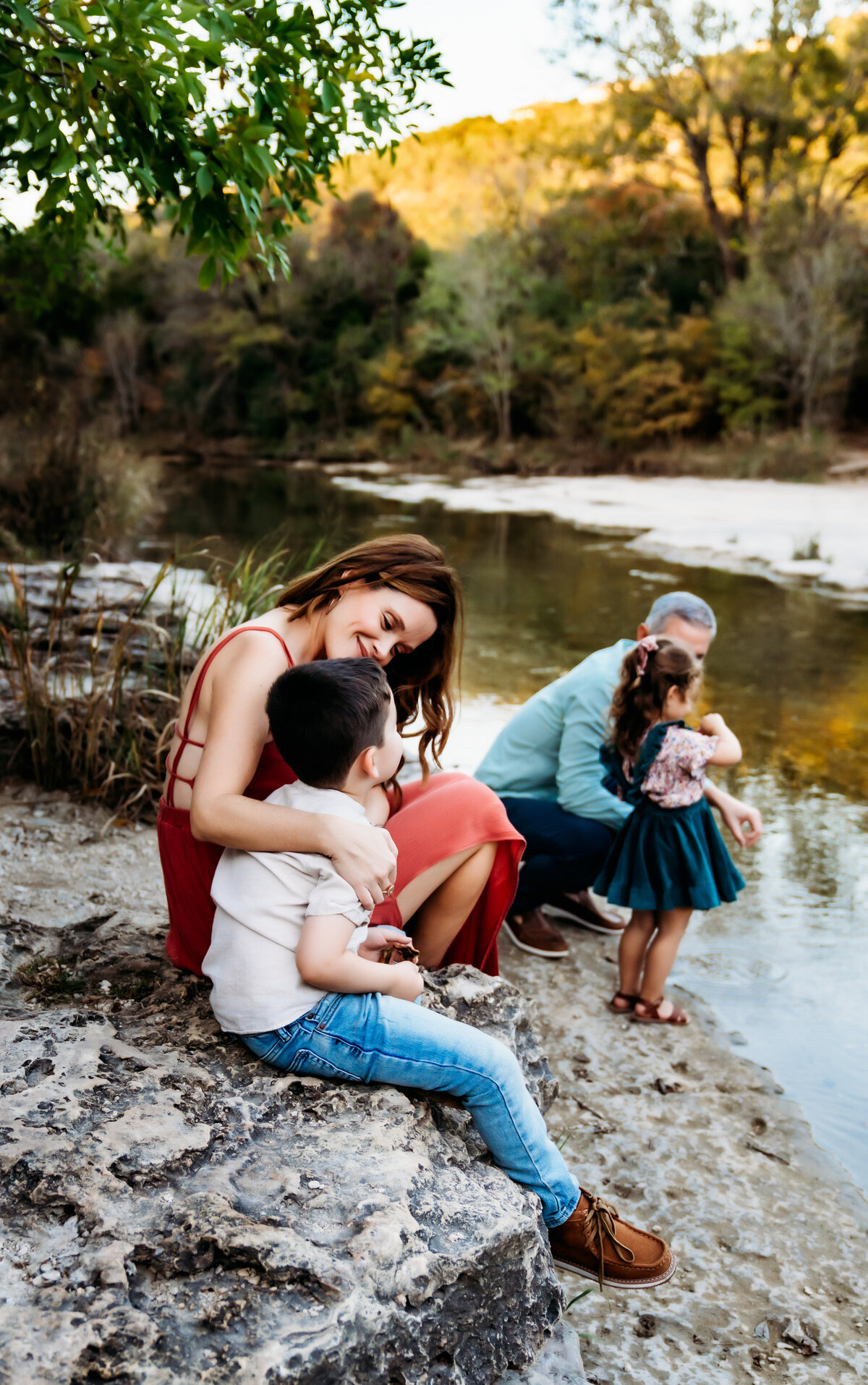 Family Photographer, a family of four sits beside the river