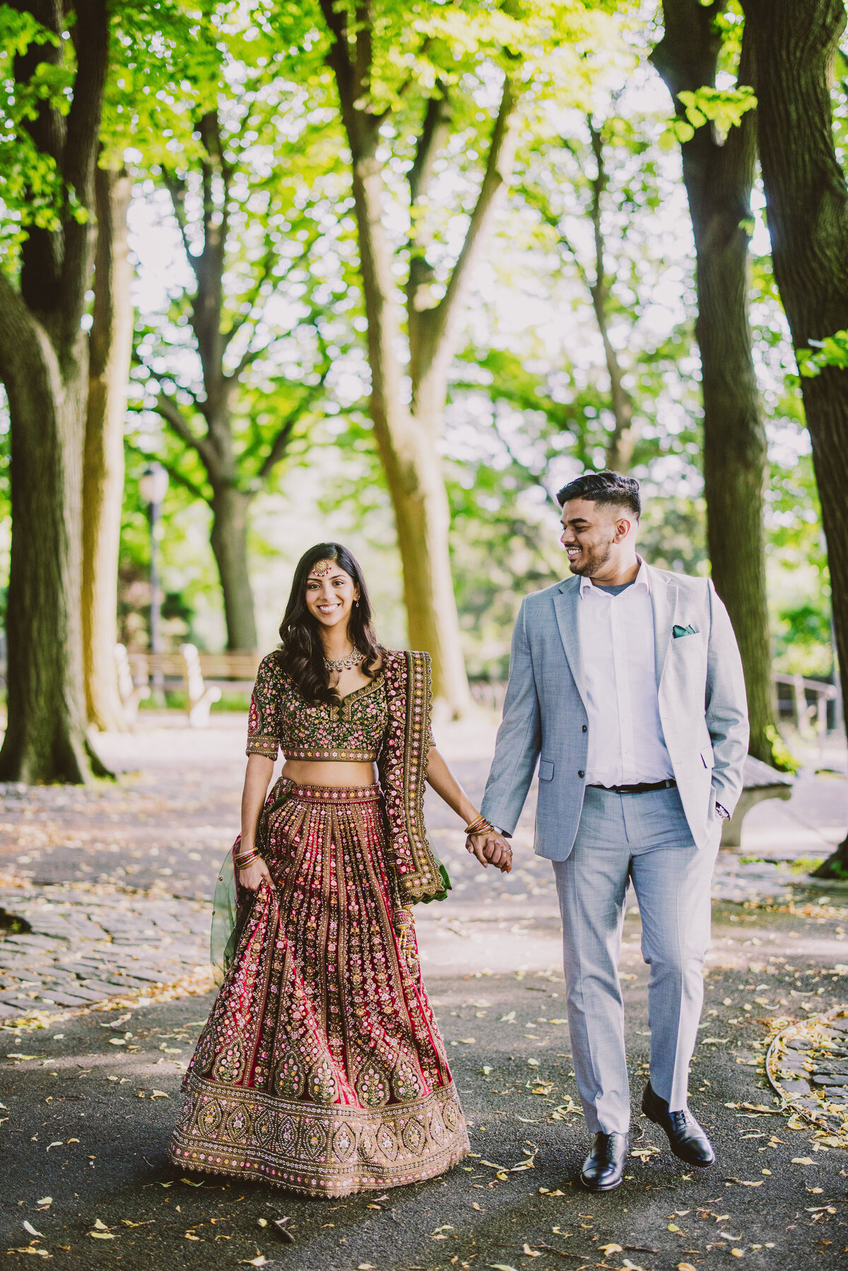 A couple wearing indian clothing and a suit walking through fort tryon park in nyc