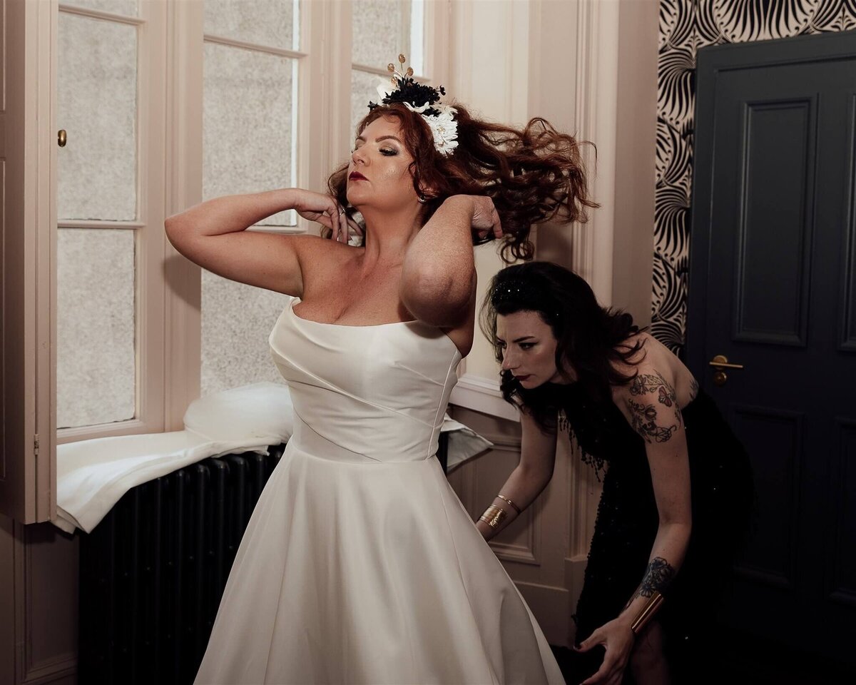 Bride and bridesmaid prepare for the wedding, the bride flicks her hair dramatically.