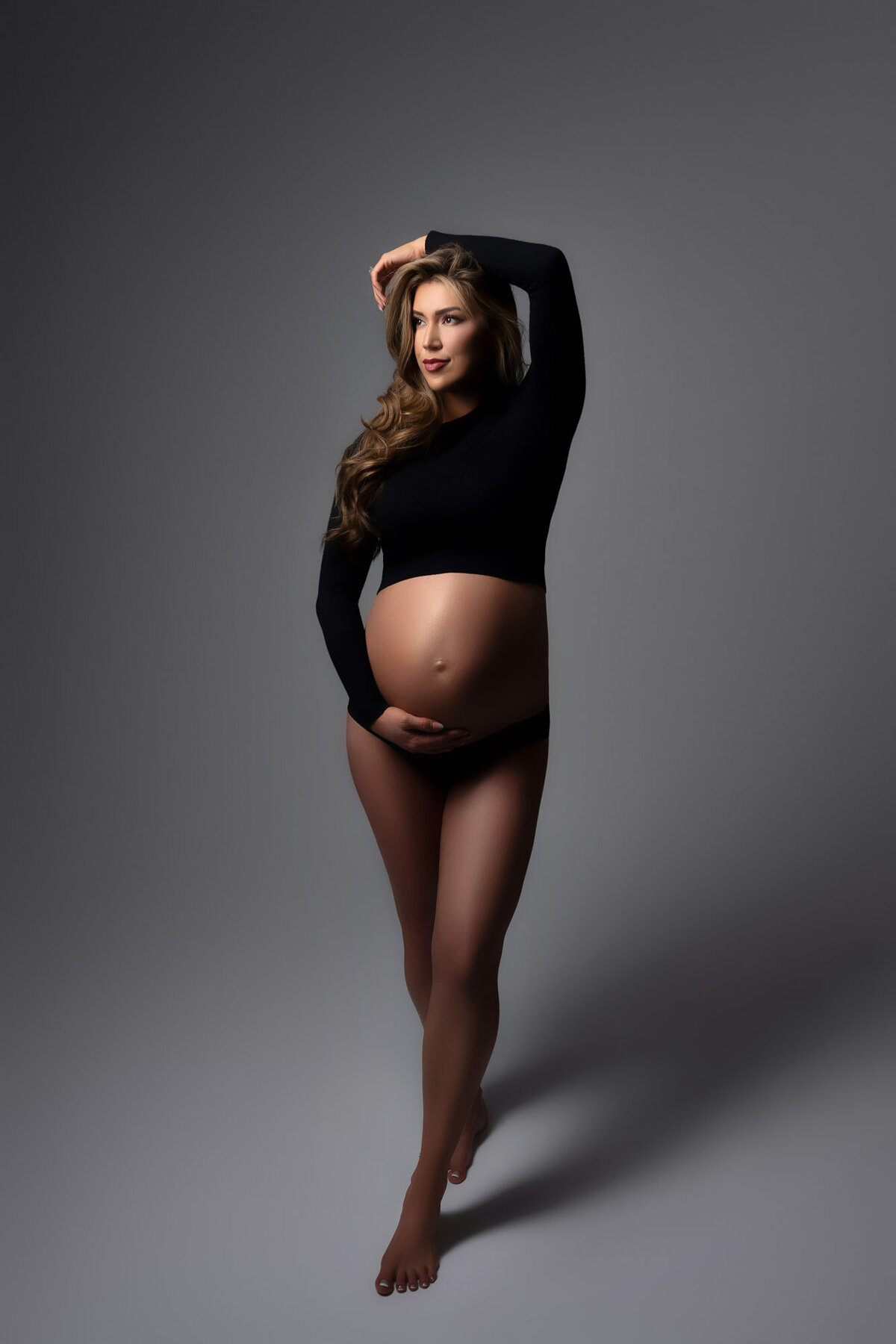 Maternity portrait of expectant mother in black outfit highlighting baby bump in studio setting