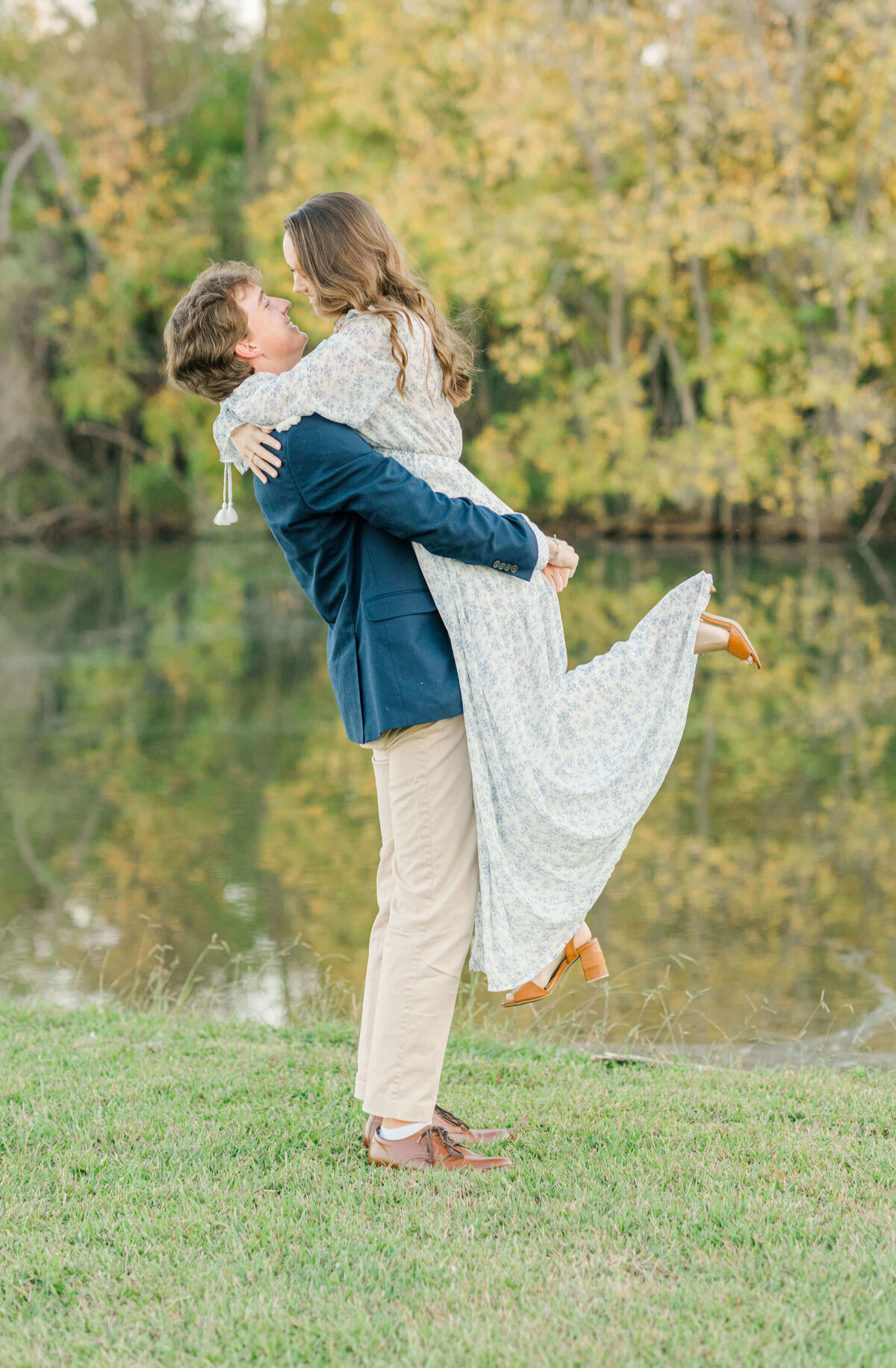 Engaged alabama couple standing in front of water while  future groom is lifting future bride up