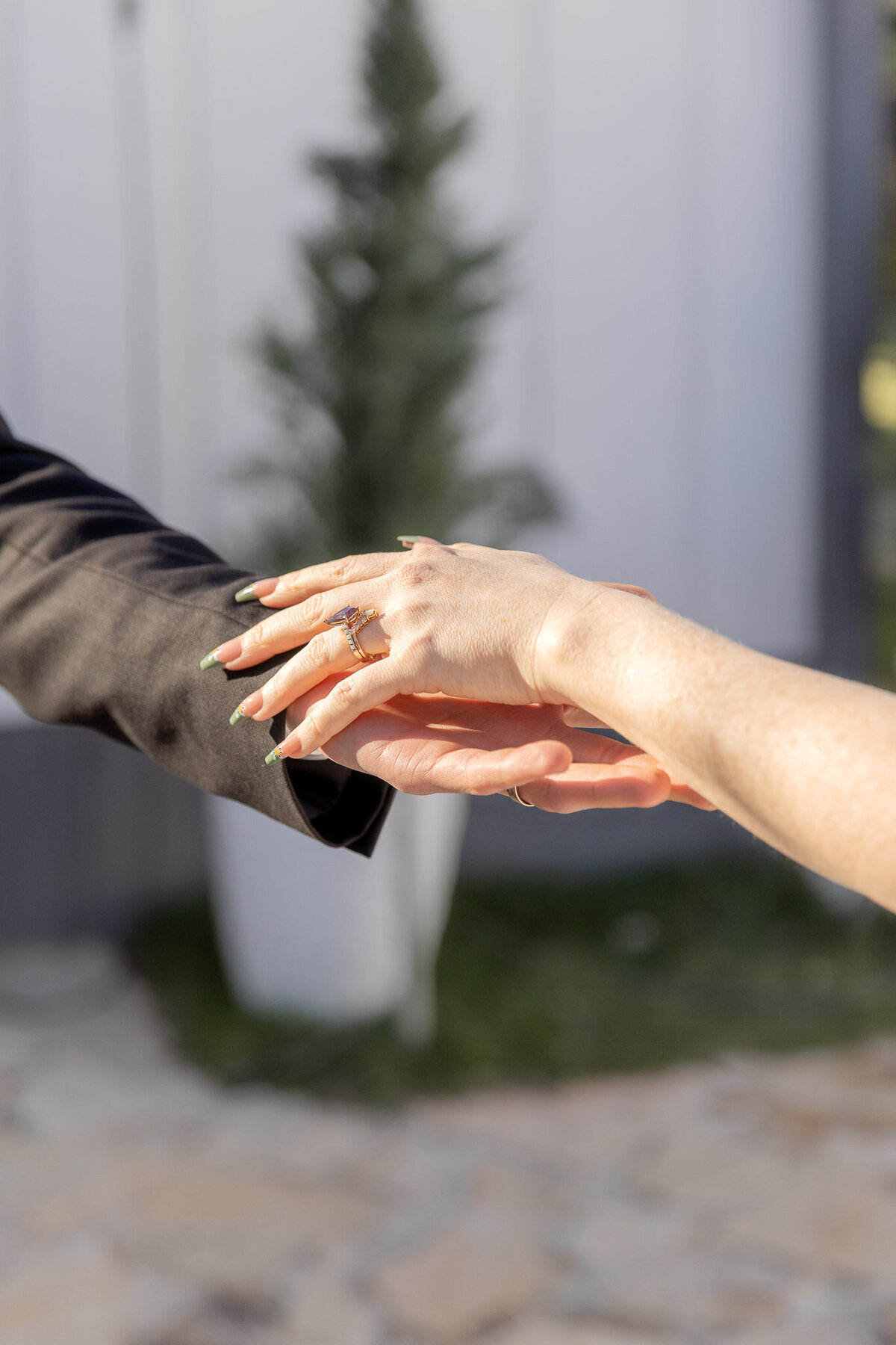 A timeless photo of a bride and groom reaching out to one another, holding hands. The photo is cropped so you can only see their hands.