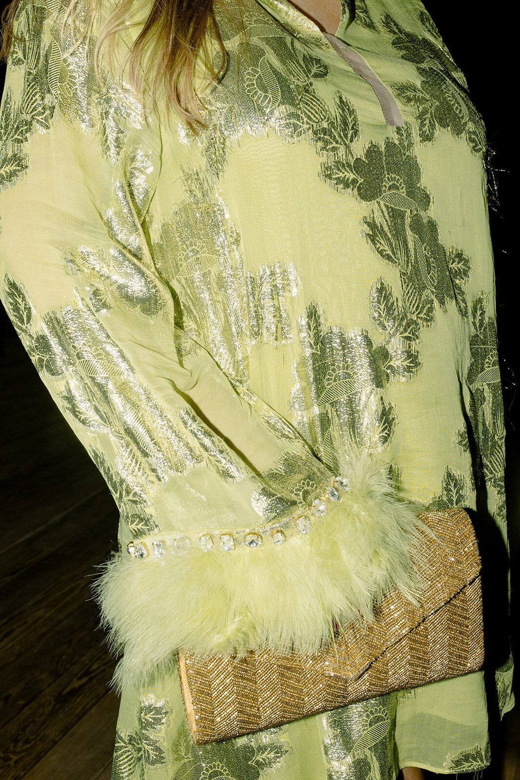 Close up of wedding guest's bright green dress with feather sleeves and a gold clutch purse