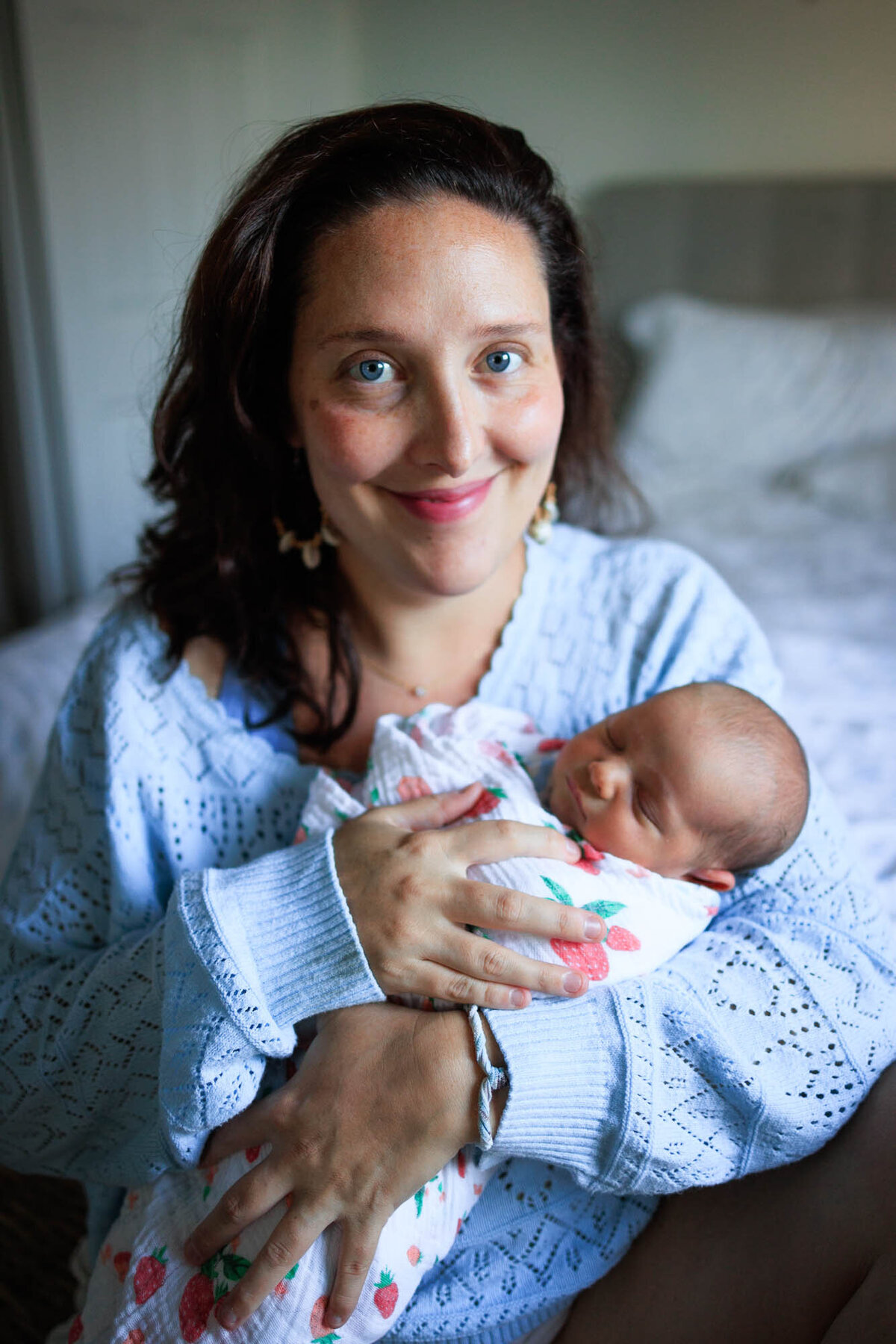 A new mom holds her newborn baby while looking at the camera and smiling.
