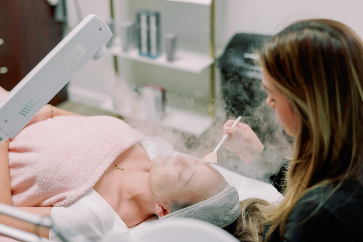 A makeup artist steams a client's face.