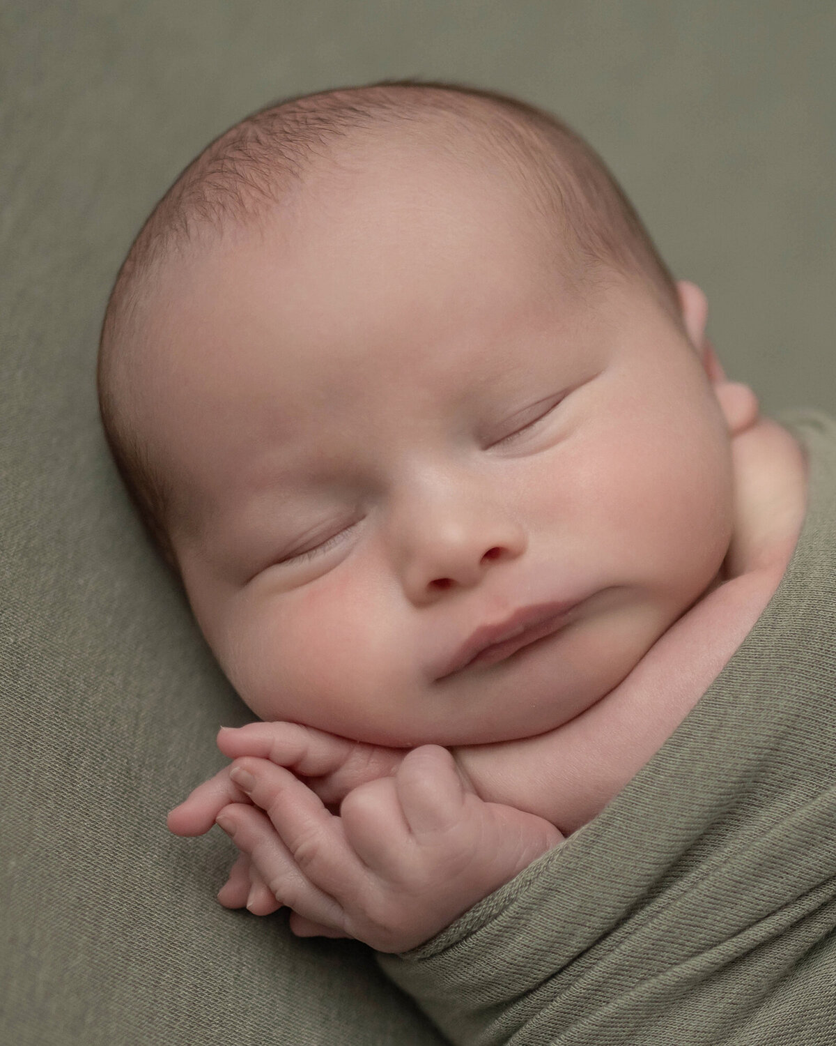 An image from a Pella Newborn Photographer of a newborn baby sleeping in a green swaddle with hands poking out