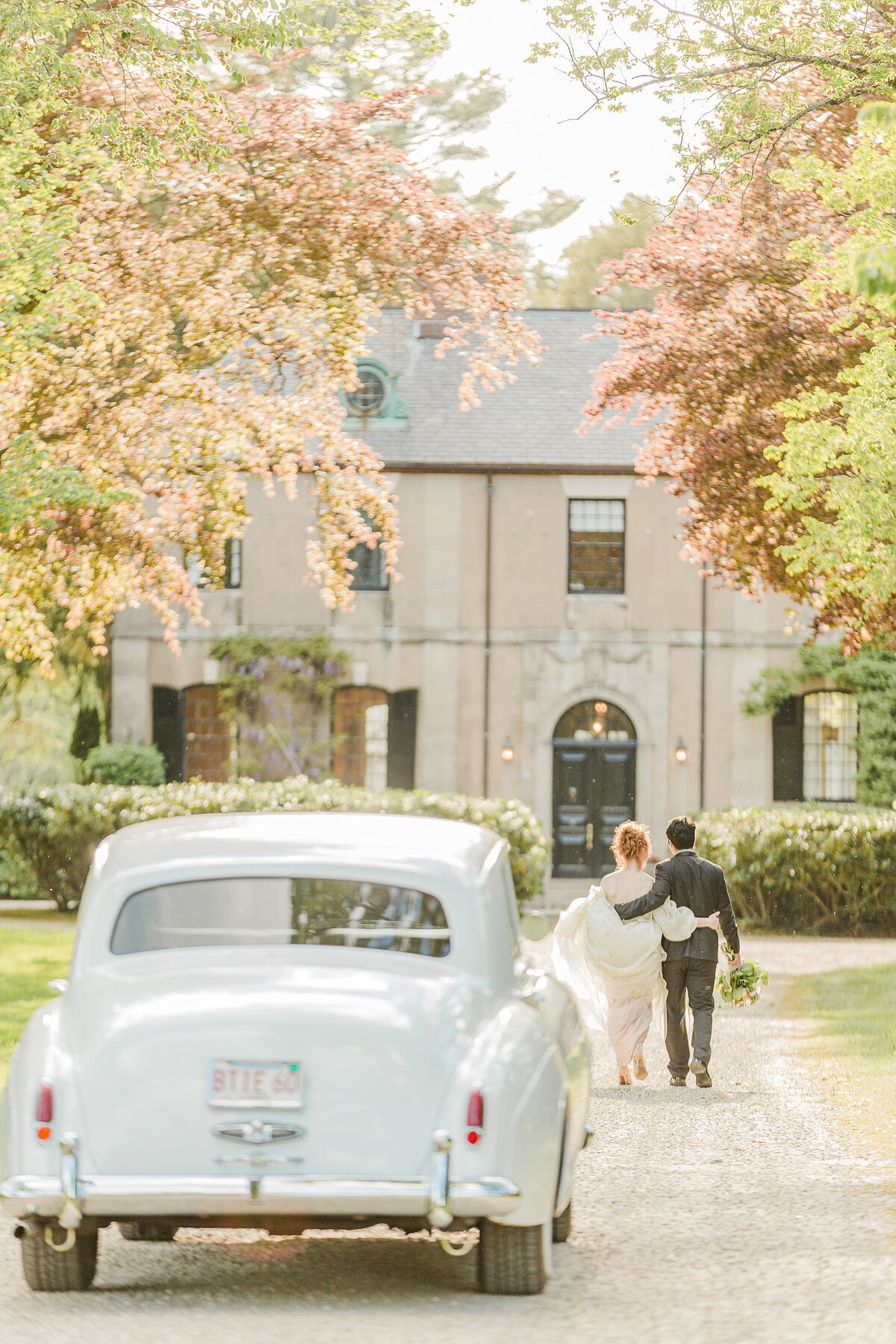 Bride and groom walk with their arms wrapped around each other towards a French chateau. A vintage Rolls Royce is in the foreground. Captured by best destination wedding and elopement photographer Lia Rose Weddings.