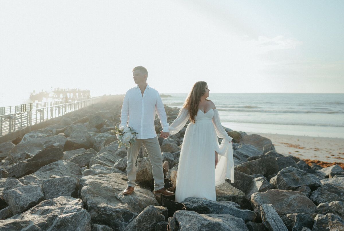 couple holding hands on coastline during wedding