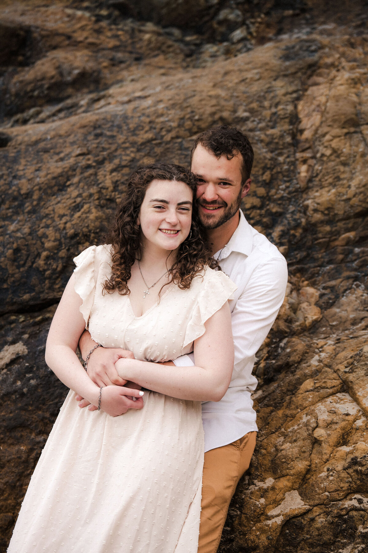engaged couple embracing by a rock wall