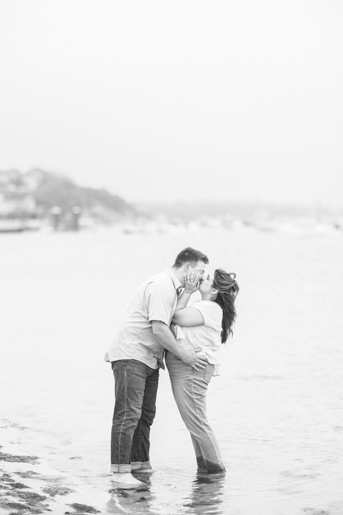 Black-and-white image of a couple standing in shallow water, kissing while holding each other close, with the harbor in the background at Chatham Bars Inn in Chatham, Massachusetts — representing the portfolio of a Cape Cod engagement photographer.