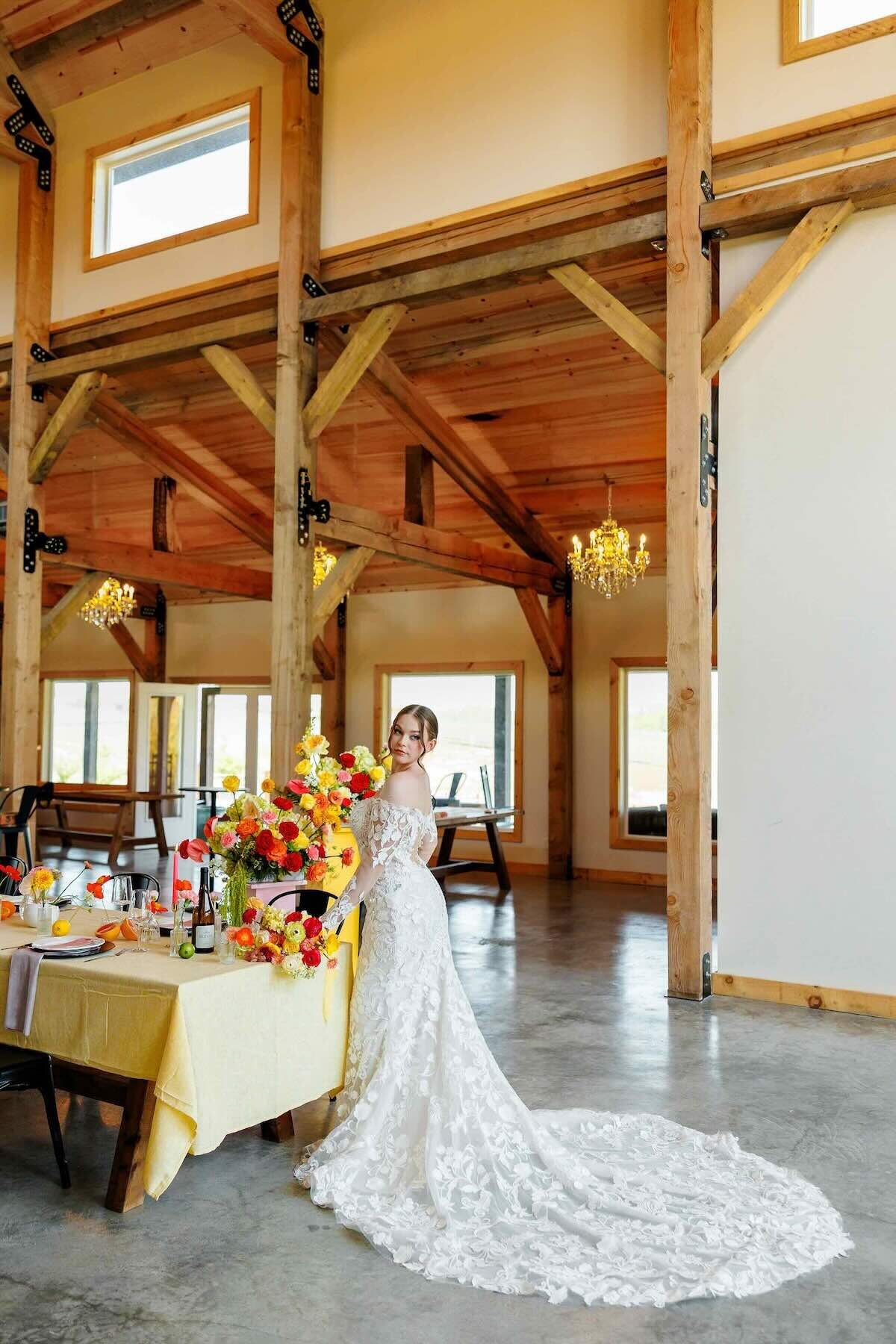 Bride in lace gown walking through a rustic modern barn venue with colorful reception setup.